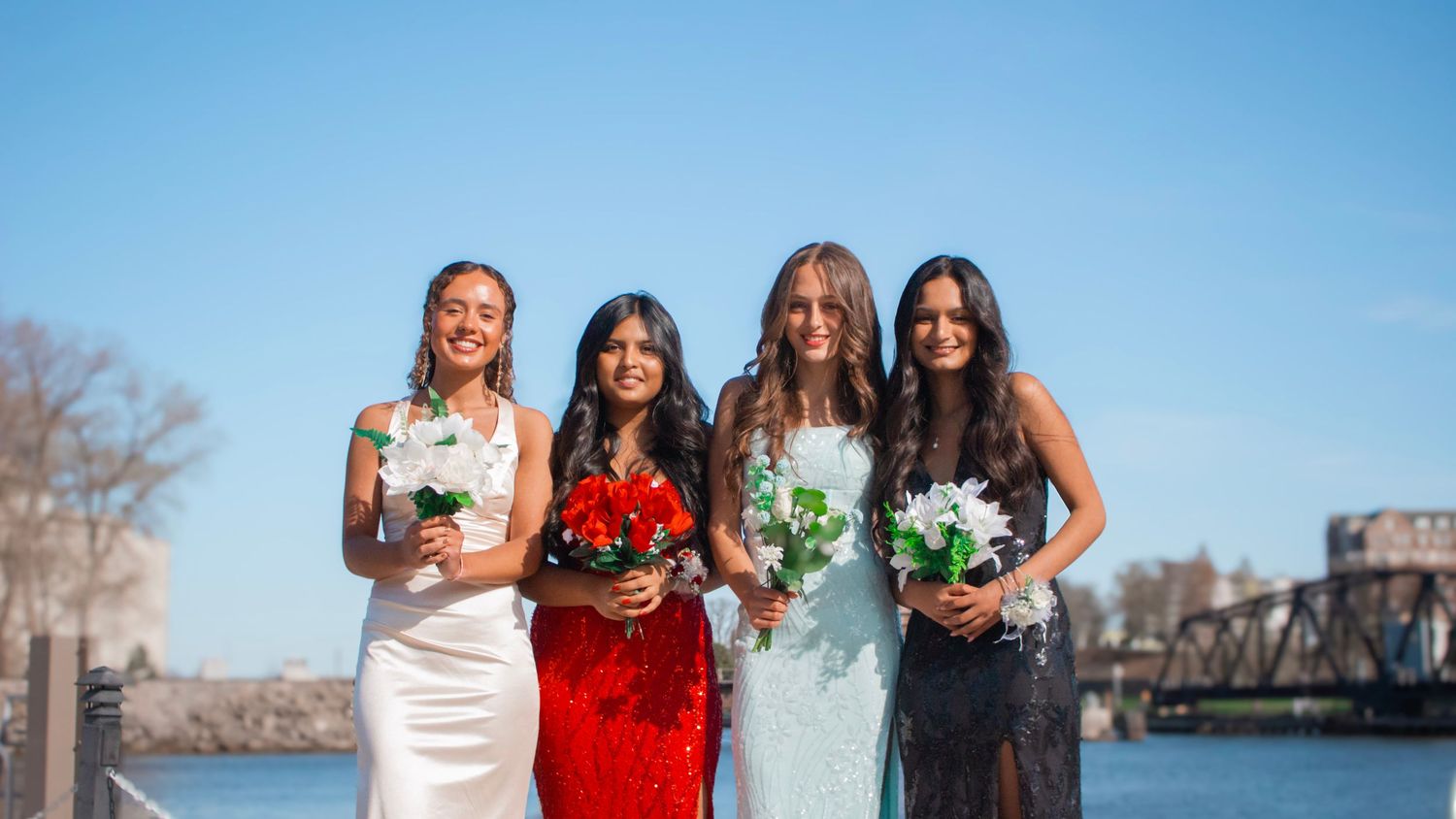 Four bridesmaids pose together holding floral bouquets against a waterfront backdrop.