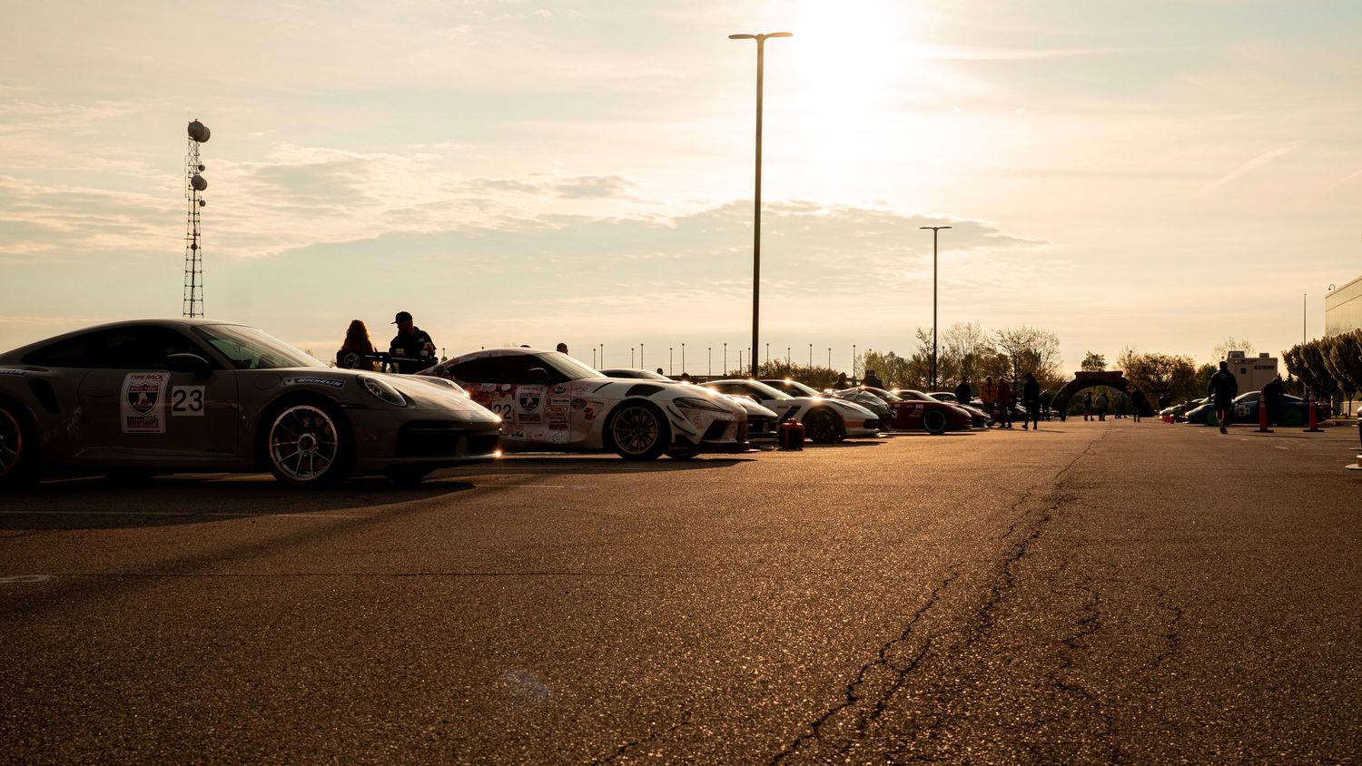 Row of sports cars parked at sunset with light pole silhouetted against sky.