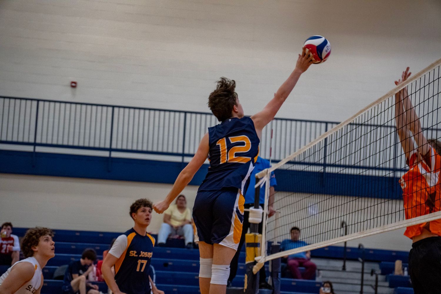 Volleyball player in navy jersey stretches to spike ball over net during game.