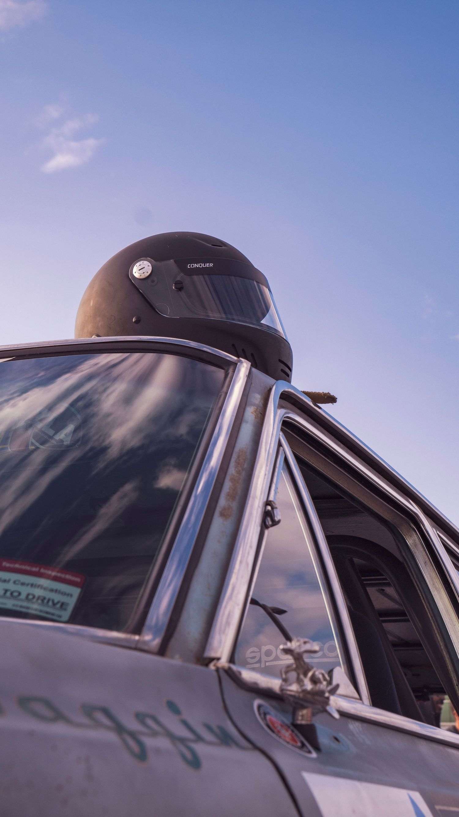 Black helmet visible through the window of a race car against blue sky.