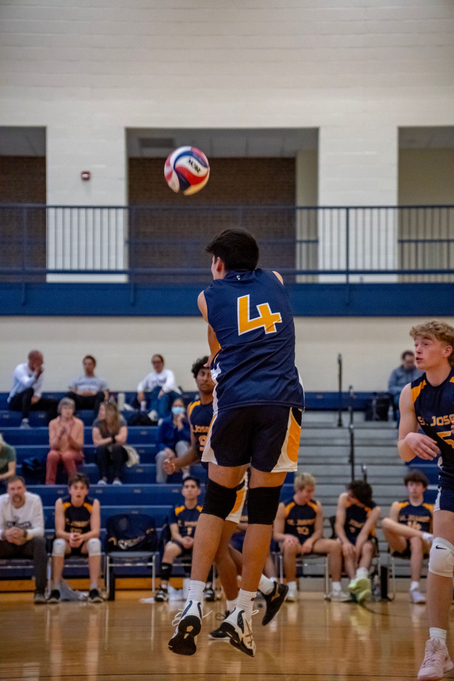 Player in navy jersey number 4 jumps to hit the volleyball during an indoor game.