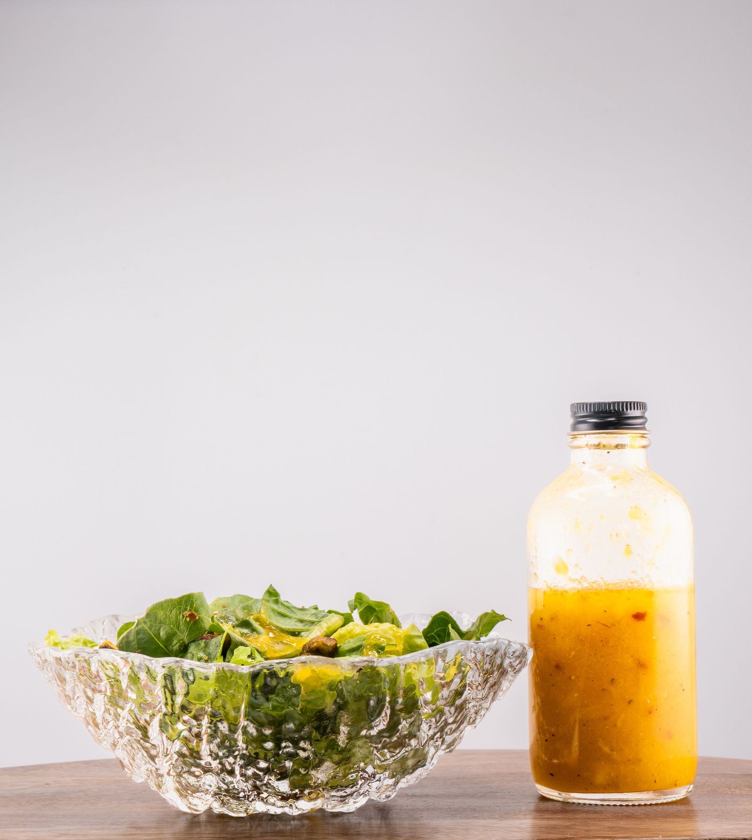 Fresh green salad in a crystal bowl next to a bottle of orange dressing.