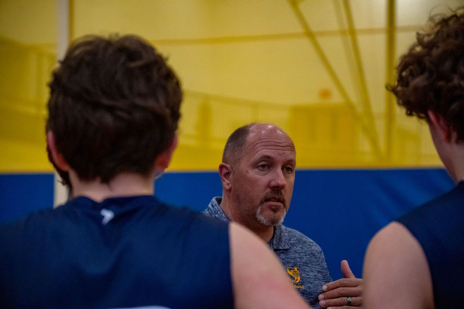 Coach discusses strategy with team members in navy uniforms during a volleyball match.