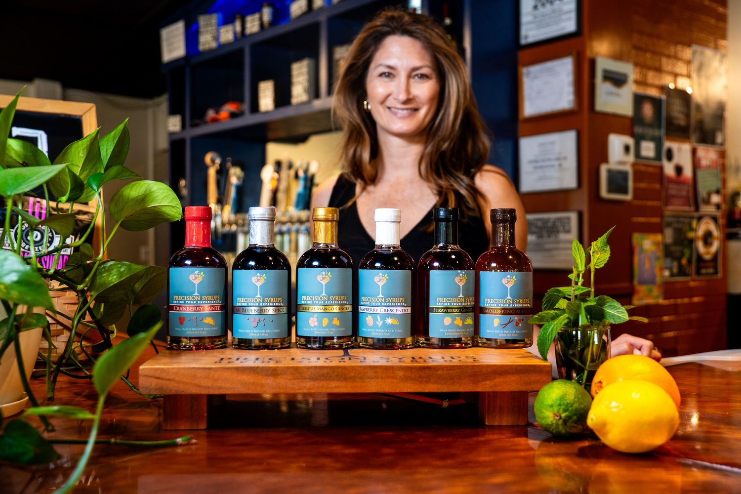 Display of botanical craft spirits with blue labels arranged on wooden bar top with citrus and plants.