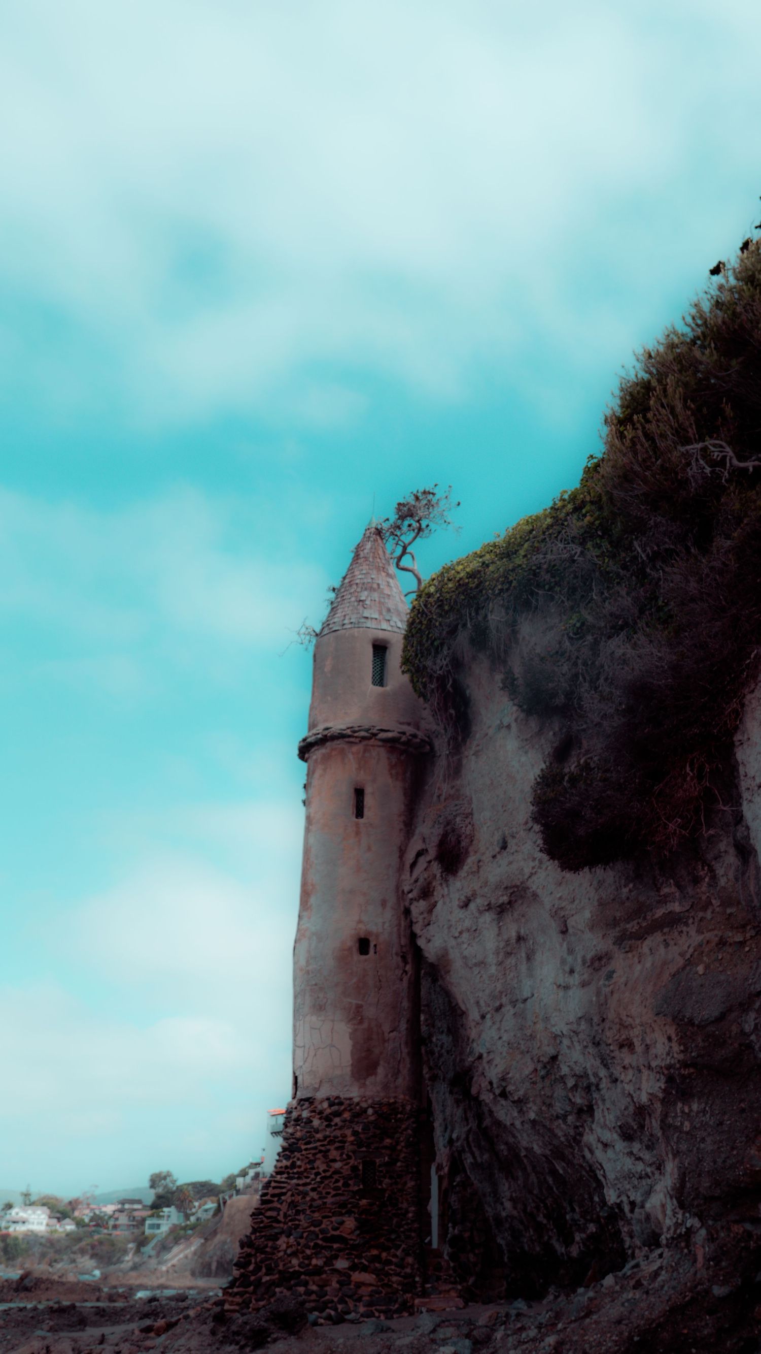 Historic lighthouse tower emerging from rocky cliff face under bright turquoise sky.