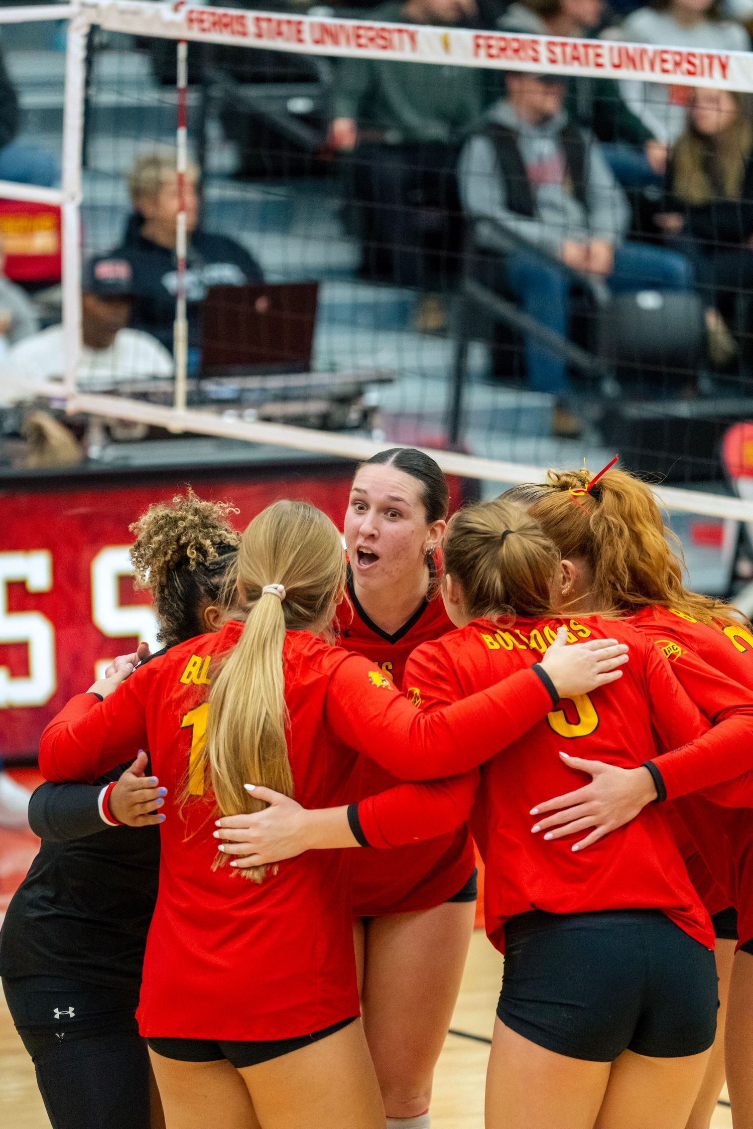 Volleyball team huddles together wearing red jerseys during a match at Ferris State University.