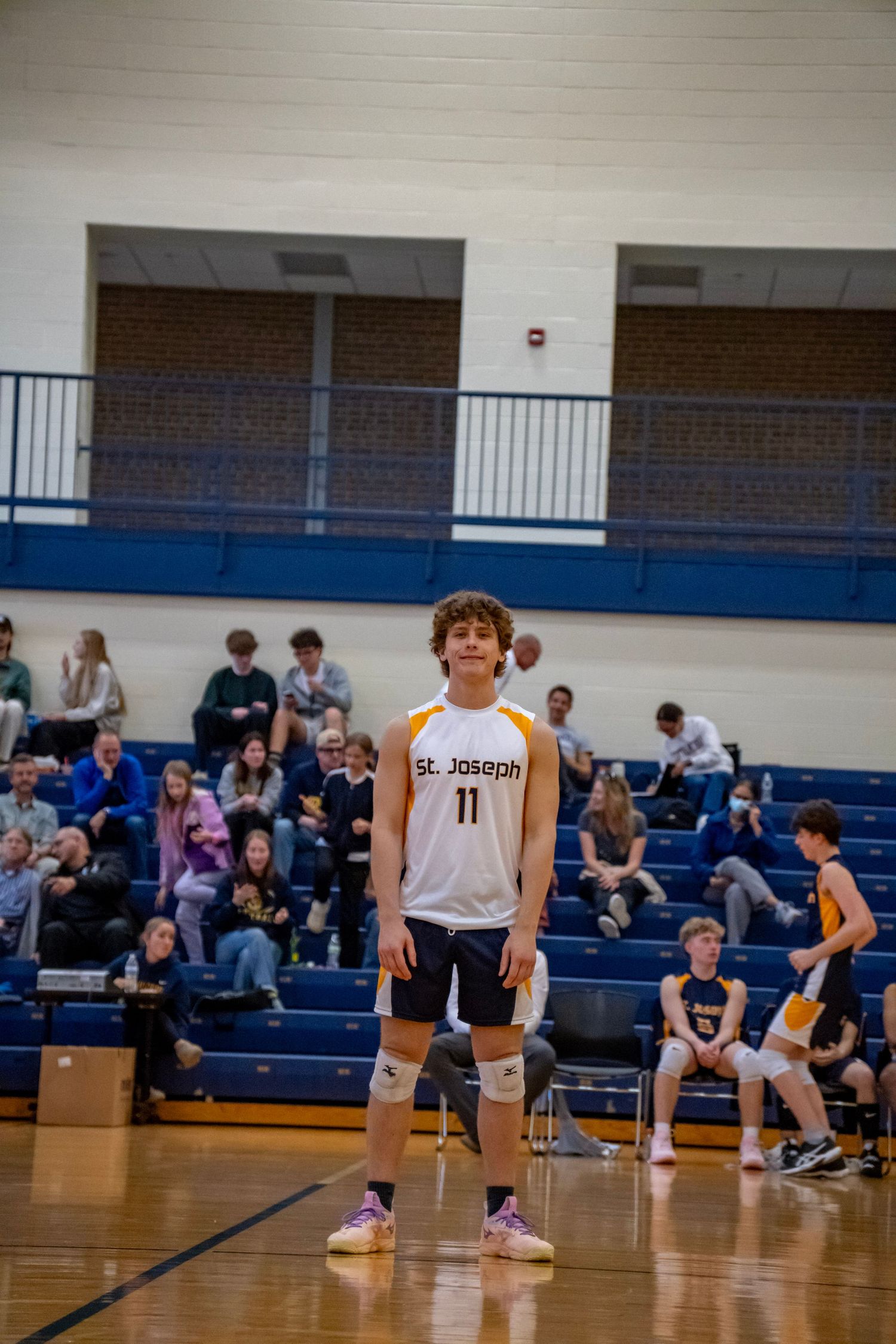 A volleyball player in a white jersey stands ready on the court during a match.