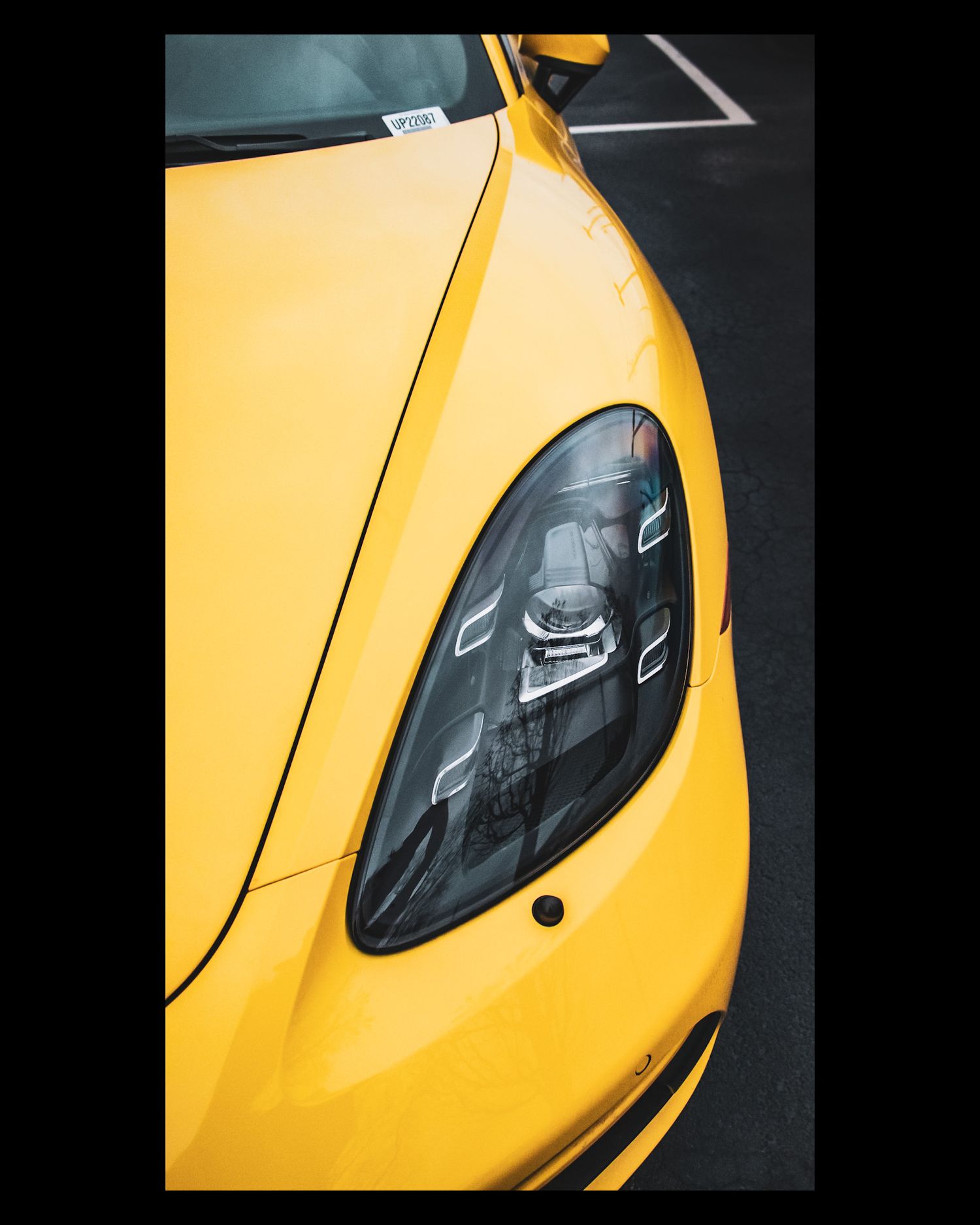 Yellow Porsche headlight detail showing sleek modern LED lighting design against dark background.