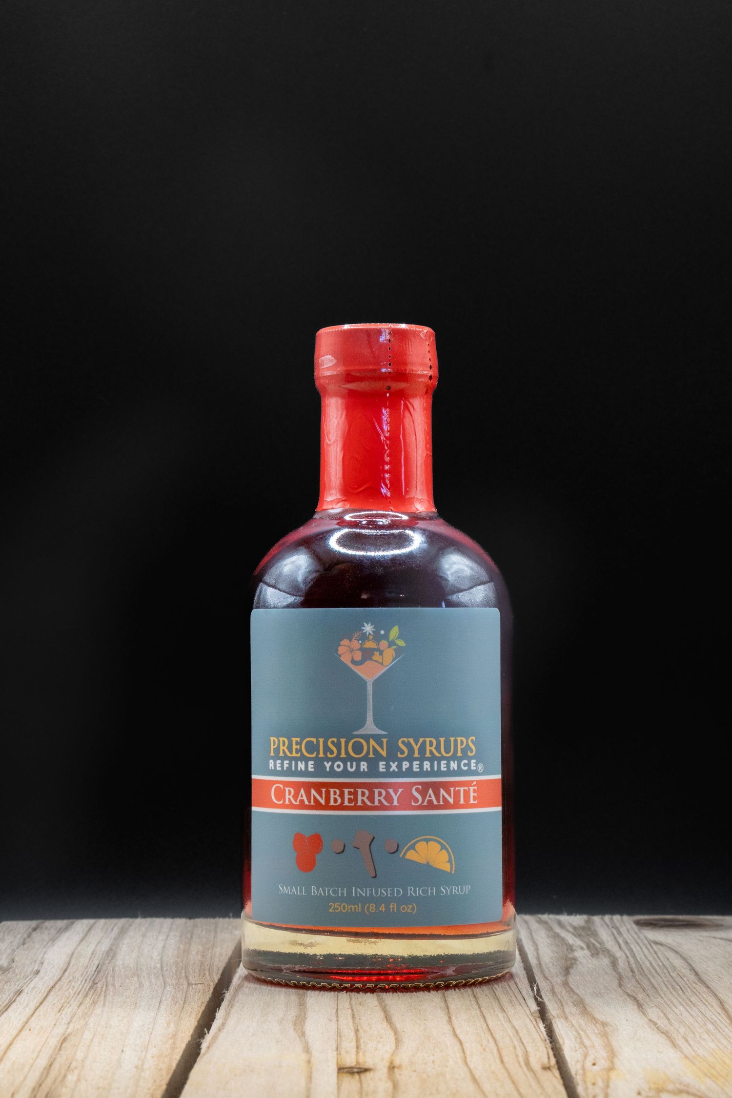 Precision Syrups cranberry syrup bottle with red cap displayed on wooden surface.