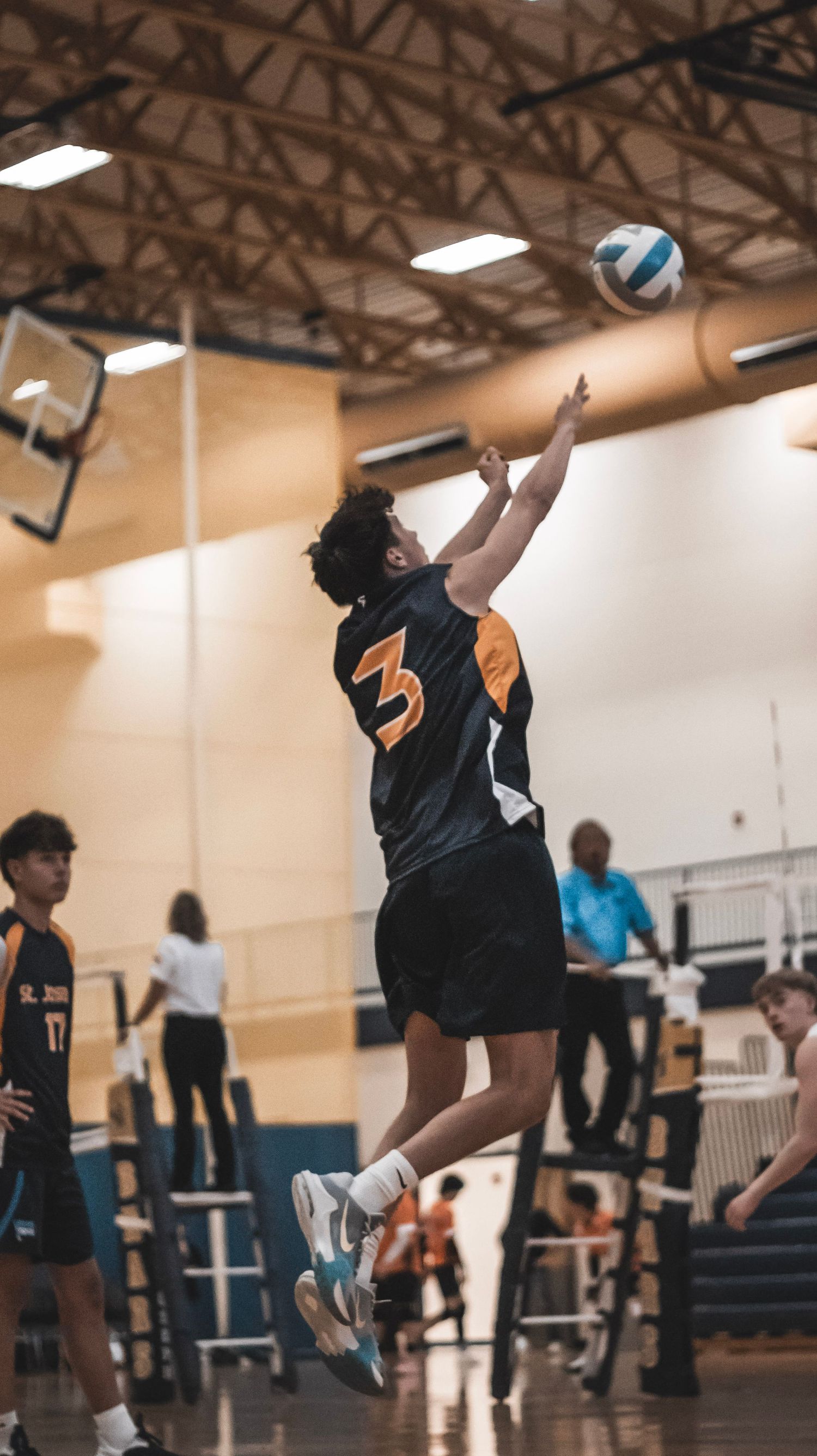 Player in black jersey number 3 jumps to hit a volleyball serve.