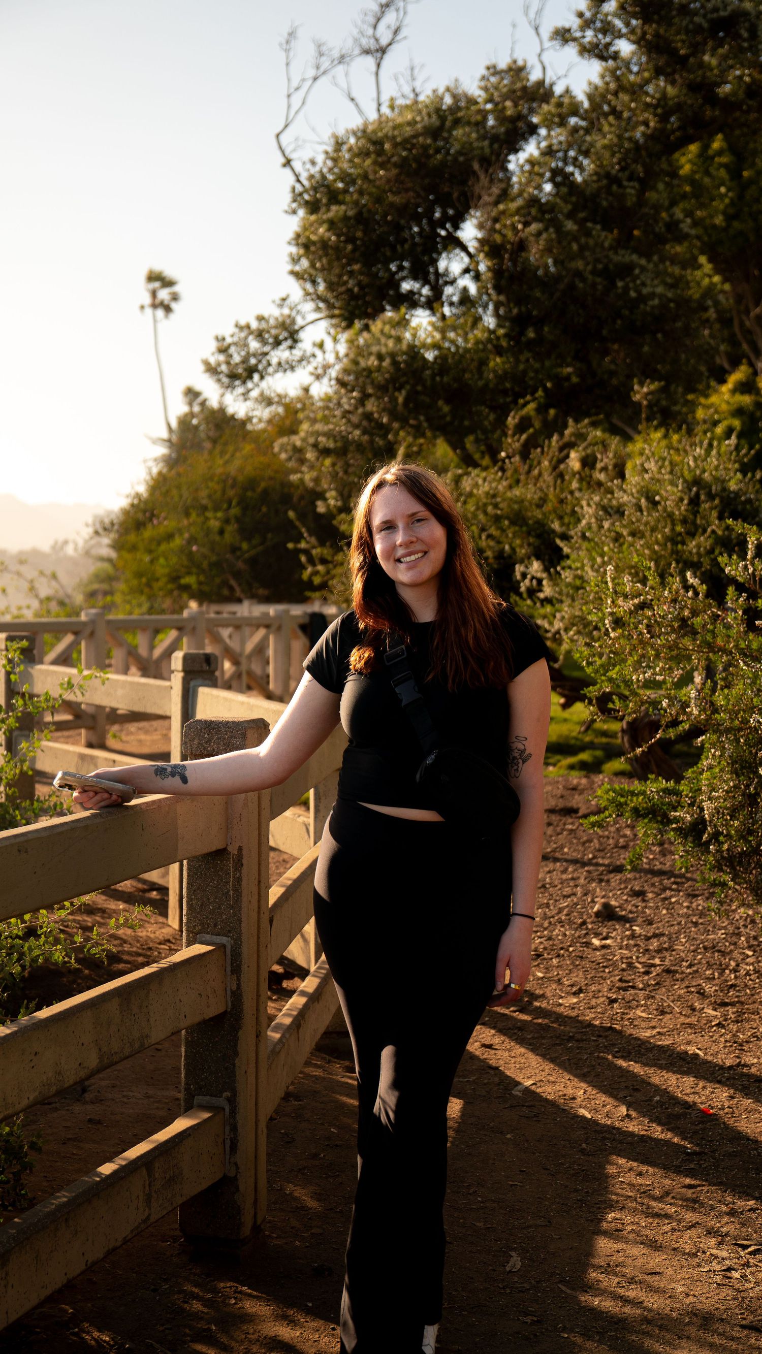 Person stands by wooden fence on nature trail during golden hour.