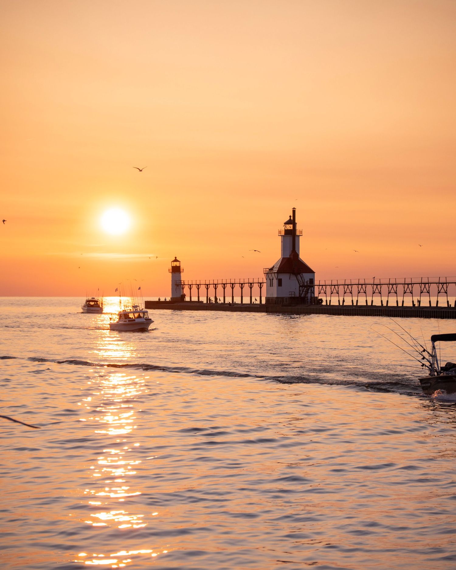Boats gather near illuminated lighthouse during golden sunset on Lake Michigan.