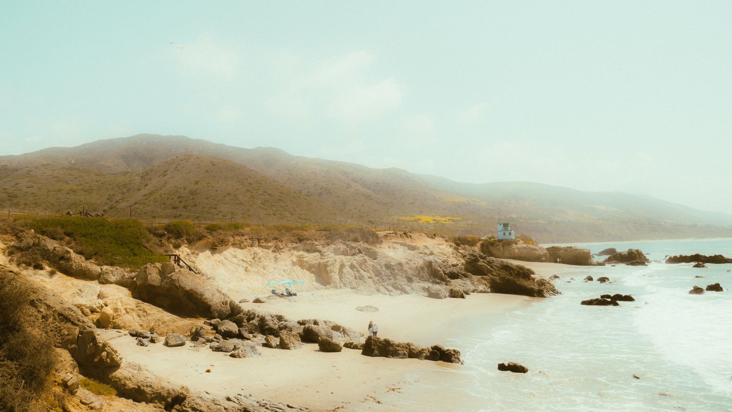 Wide panoramic view of a desert-like coastal landscape with distant ocean waves.