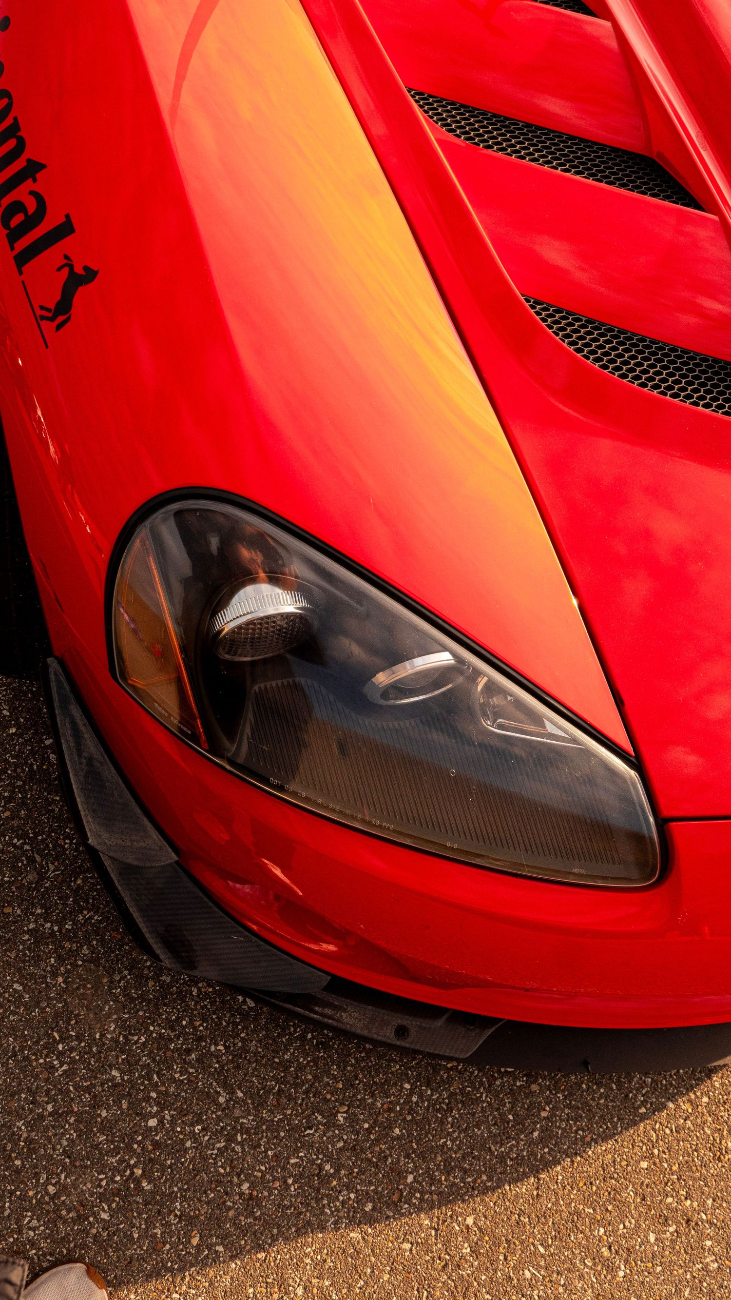 Close-up view of a red sports car headlight and hood detail with black mesh vents.