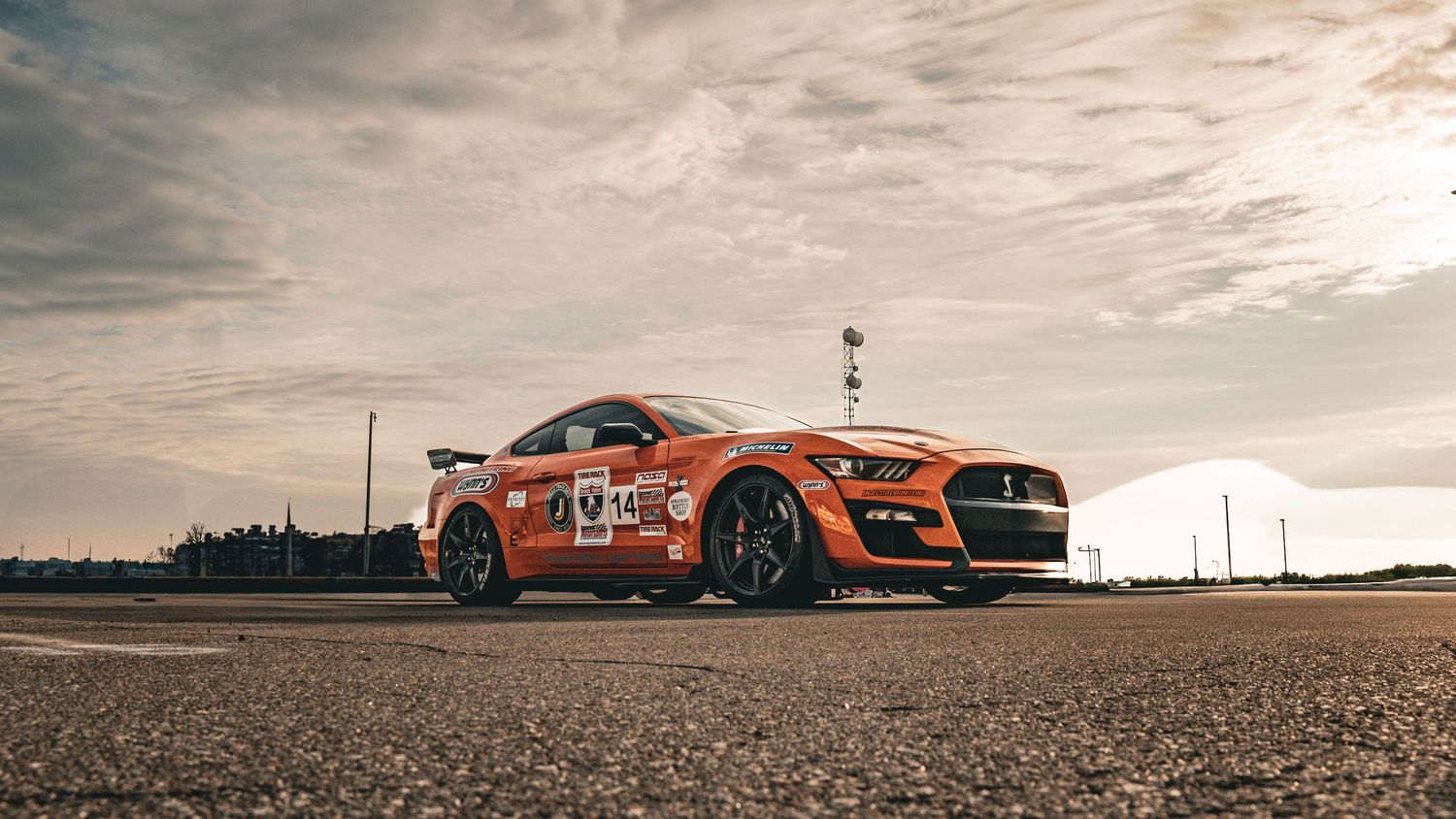 Orange Mustang Shelby GT500 race car shot at sunset on empty racing track.