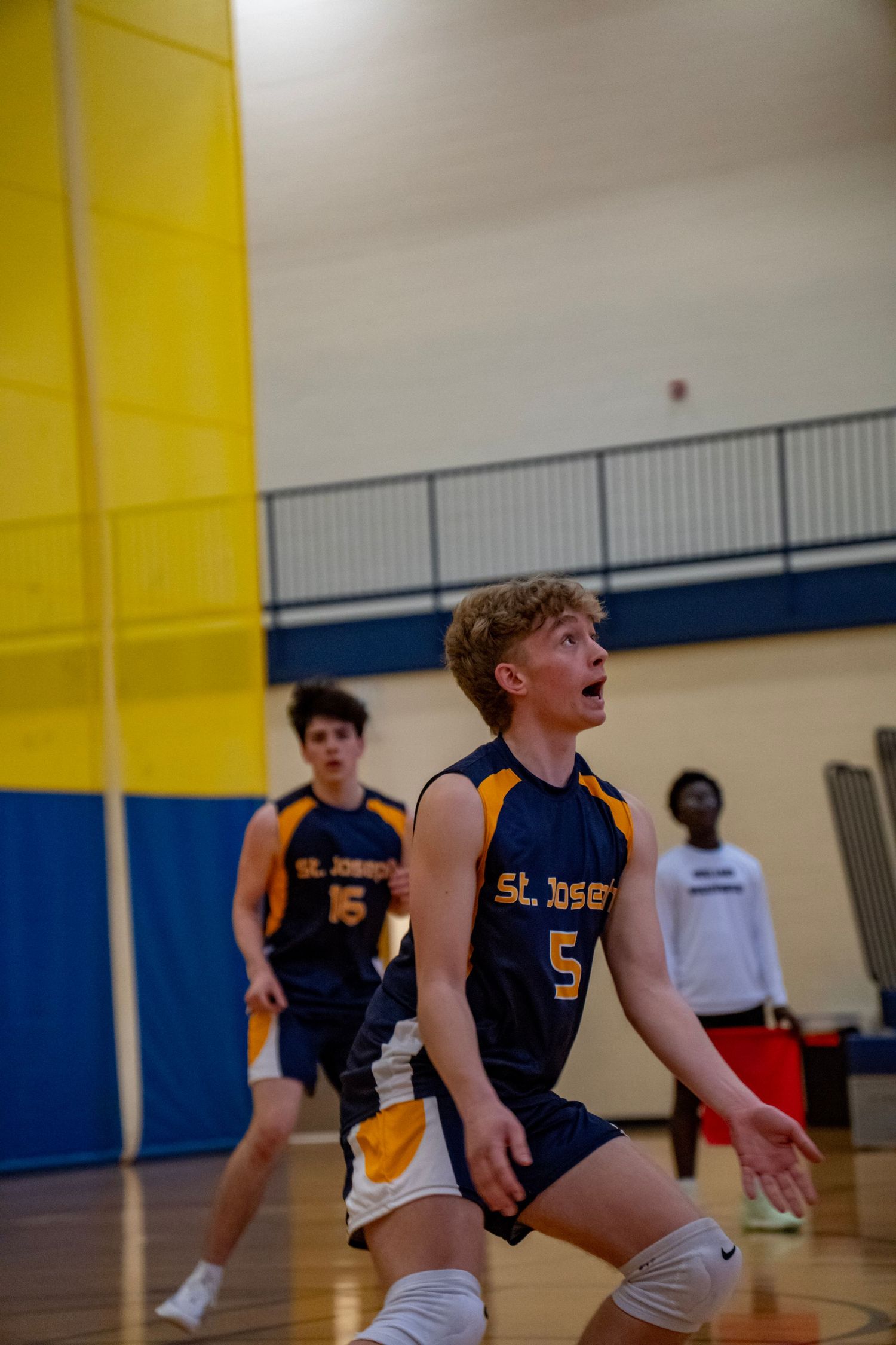 Player in navy jersey shows intense focus during volleyball game in school gym.