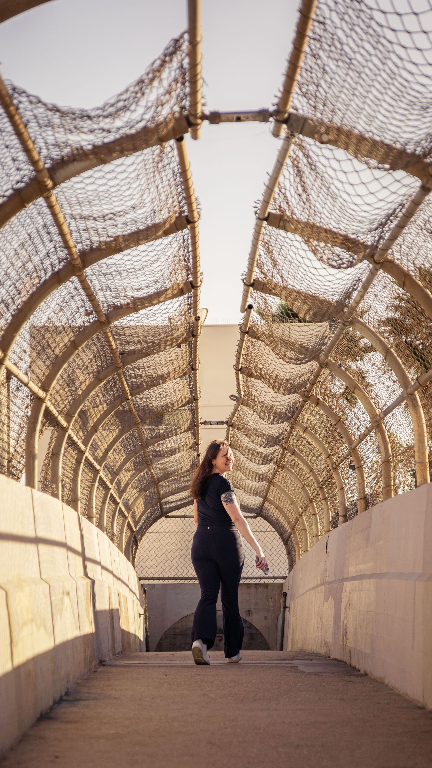 Person walking through curved tunnel corridor with mesh ceiling and white walls.