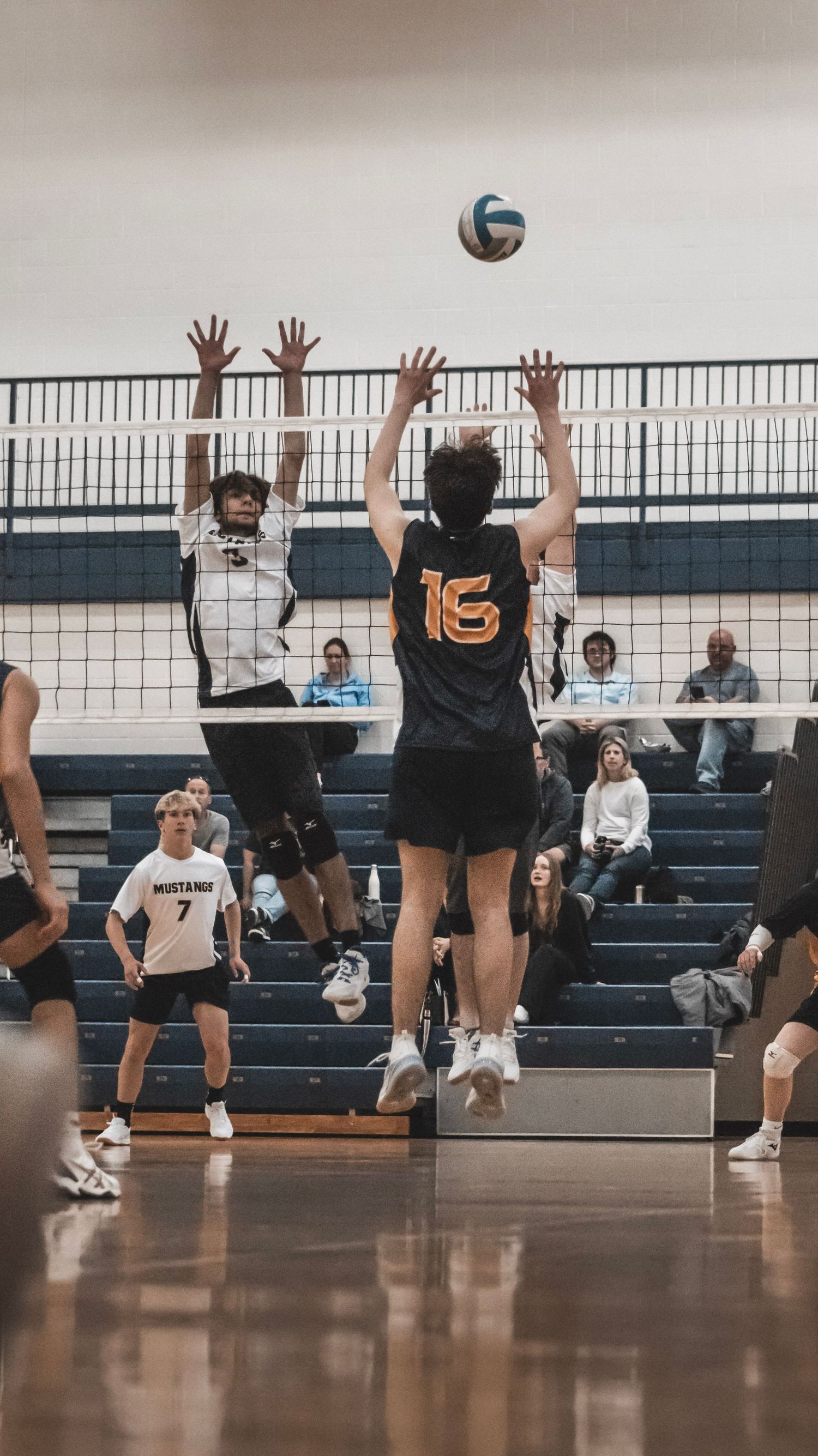 Two players jump at volleyball net for block during competitive match.