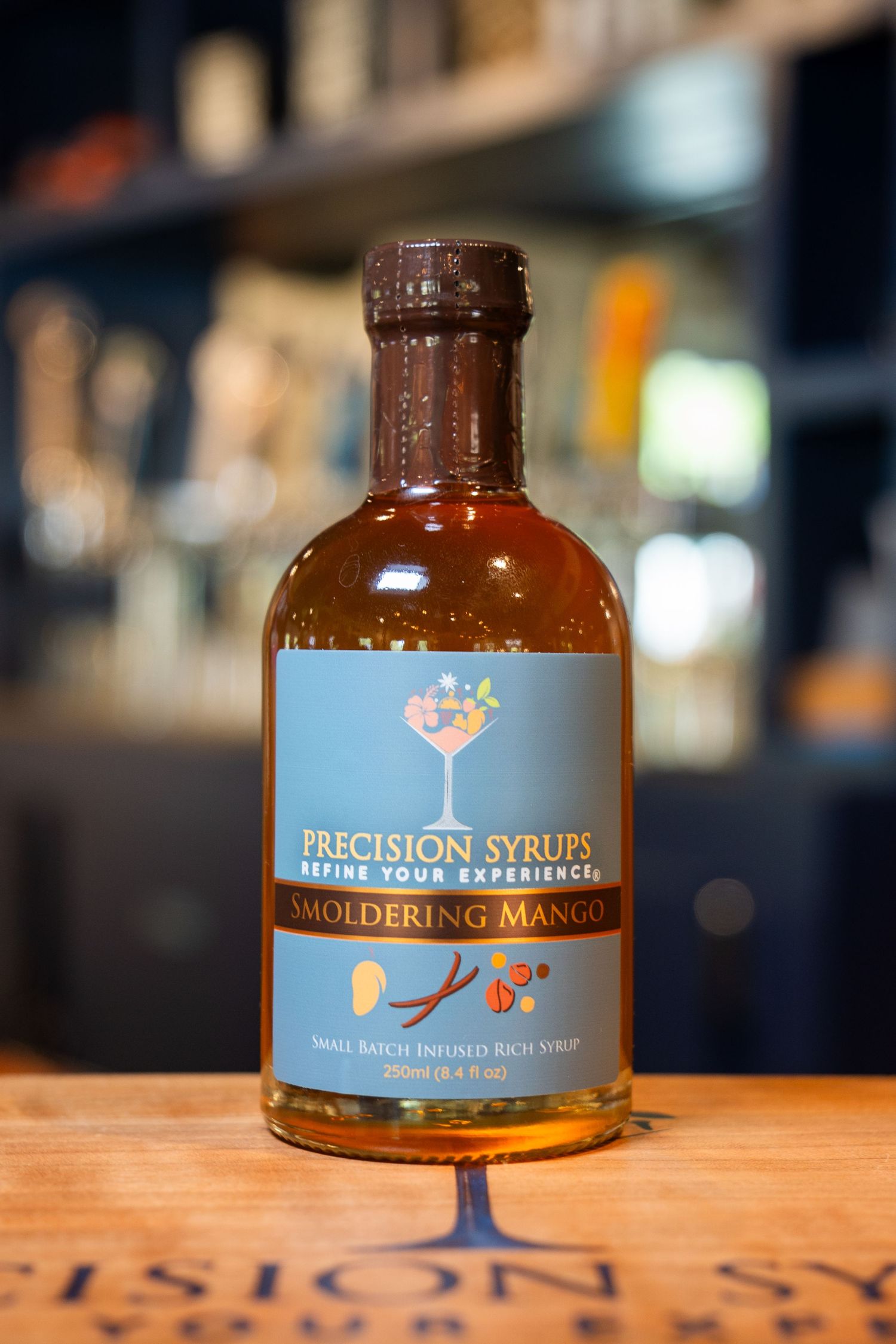 Close-up of Precision Syrup bottle with blue label on wooden bar surface.