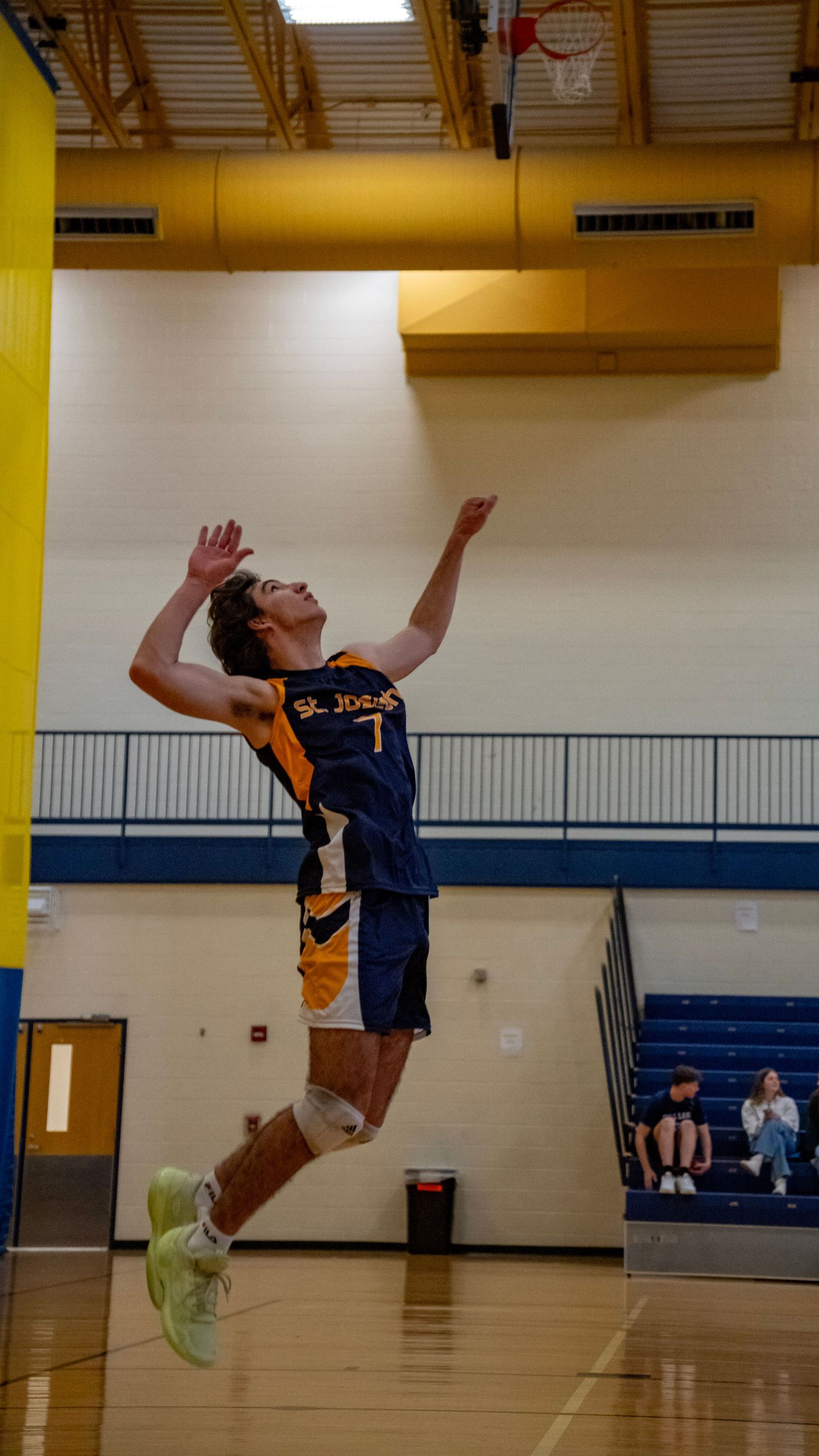 High school volleyball player in navy uniform leaps high in the air during indoor match.