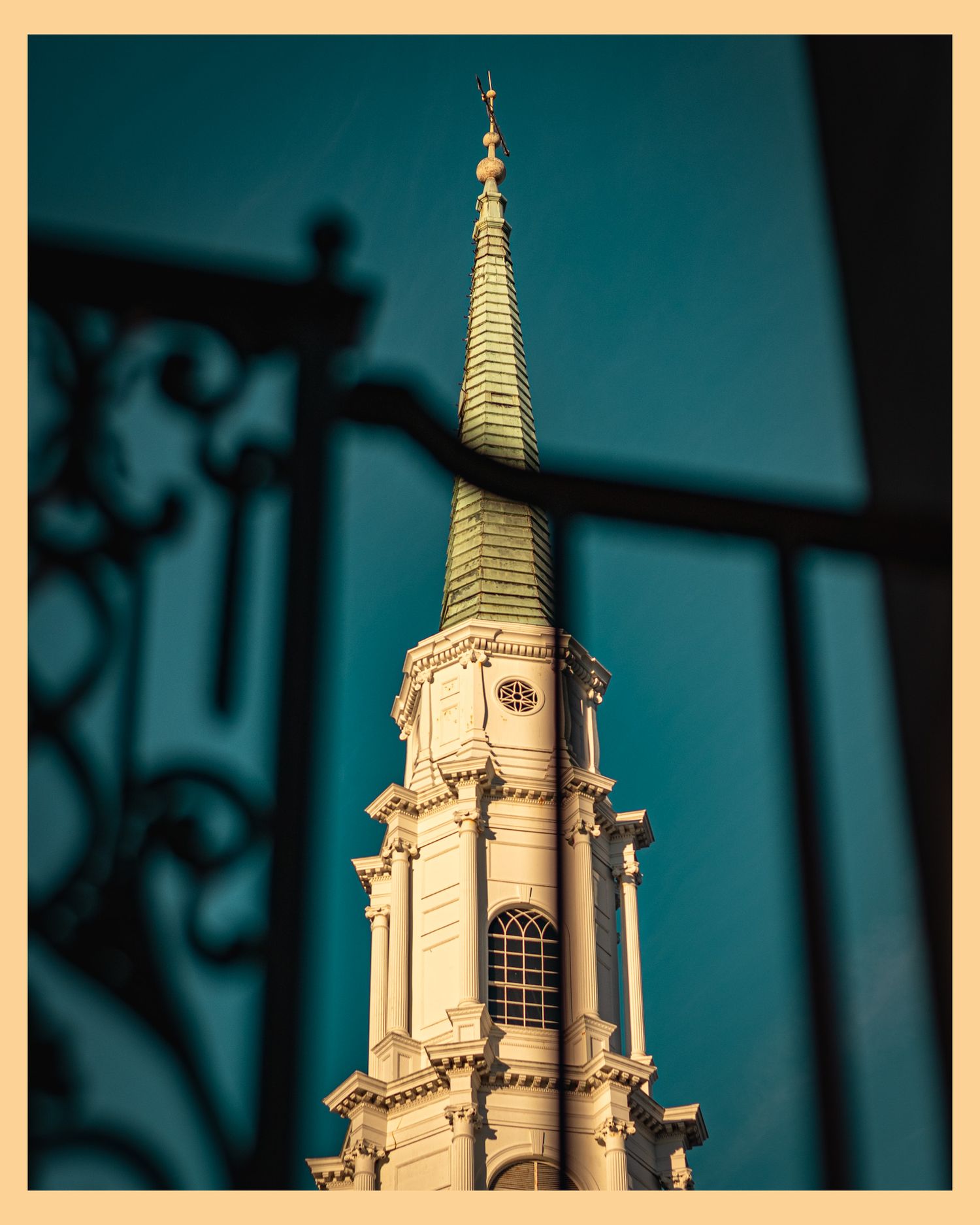 White church spire photographed through decorative iron railing against teal sky.