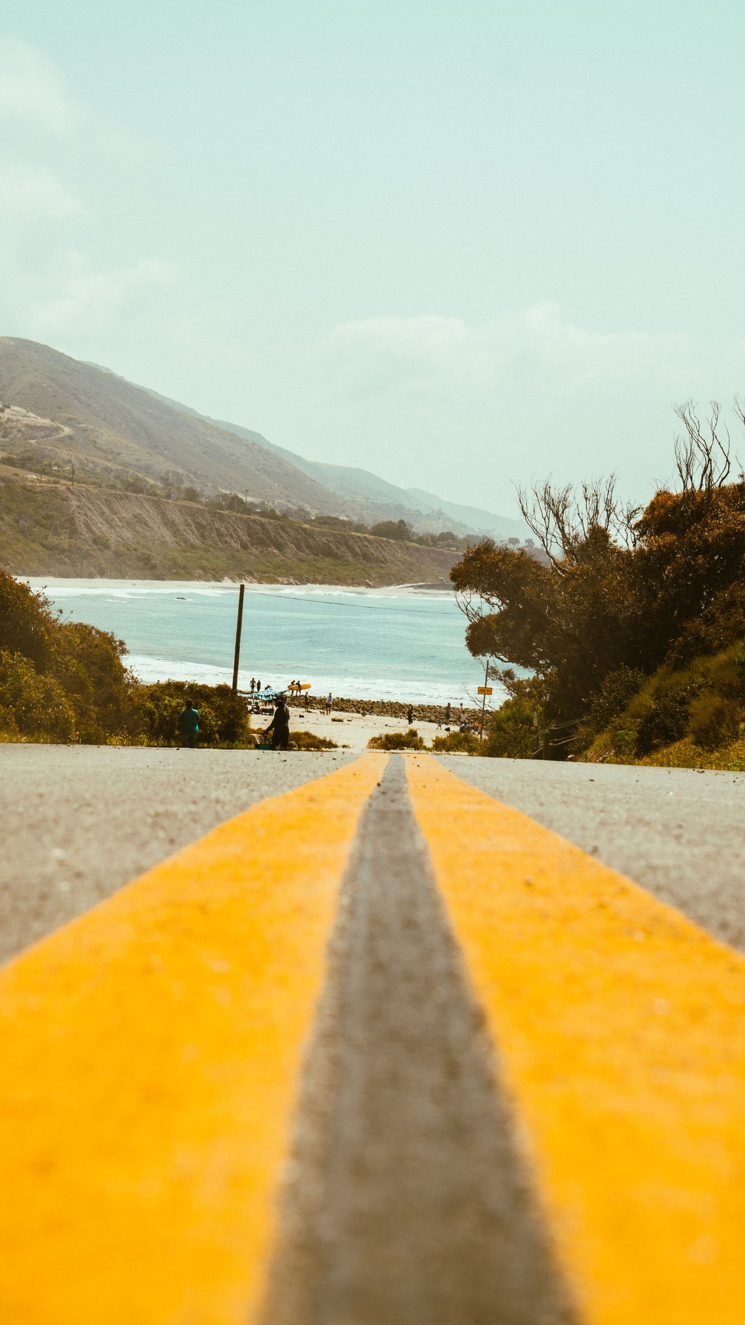 Yellow road marking leads toward ocean view with coastal mountains in the background.