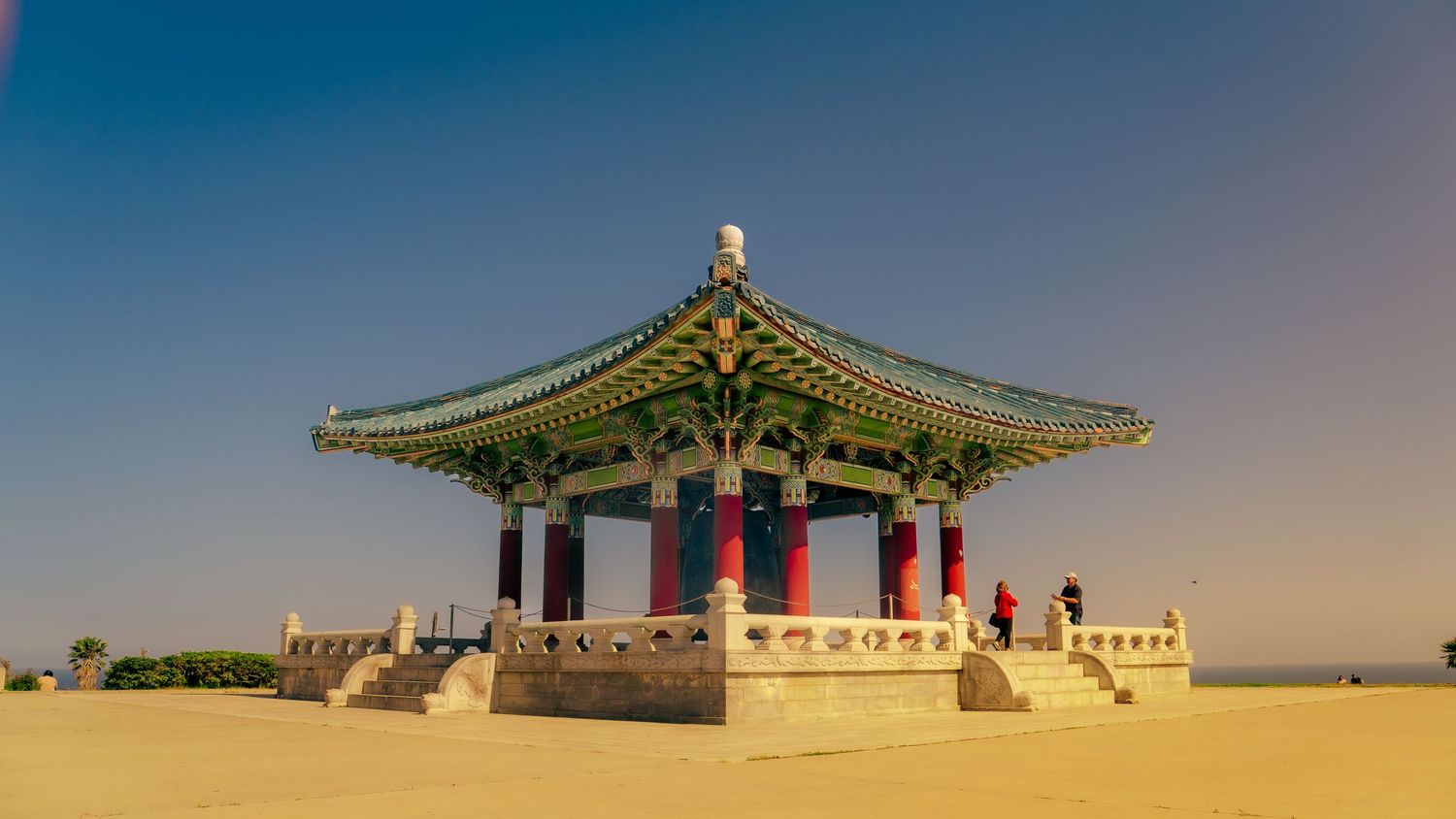 Korean bell pavilion with distinctive curved green roof and red columns photographed from side angle.