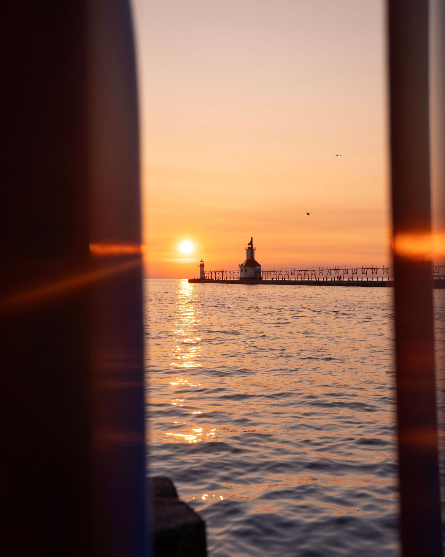 St. Joseph lighthouse and pier silhouetted against a dramatic orange sunset.