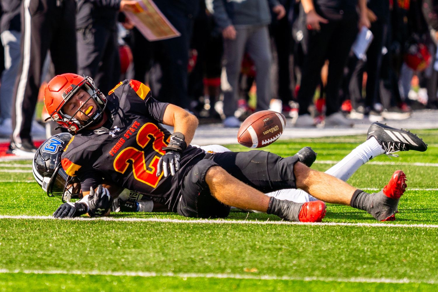 Football players lay exhausted on the field after an intense game at a crowded stadium.