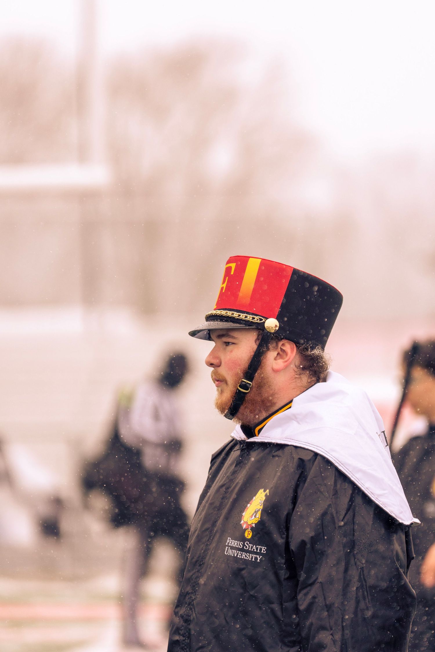 Two coaches wearing black jackets and baseball caps stand together on a sports field during practice.
