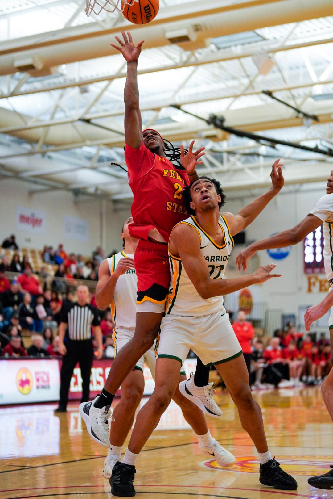 Basketball players leap and stretch to grab a loose ball during an intense game in a high school gymnasium.