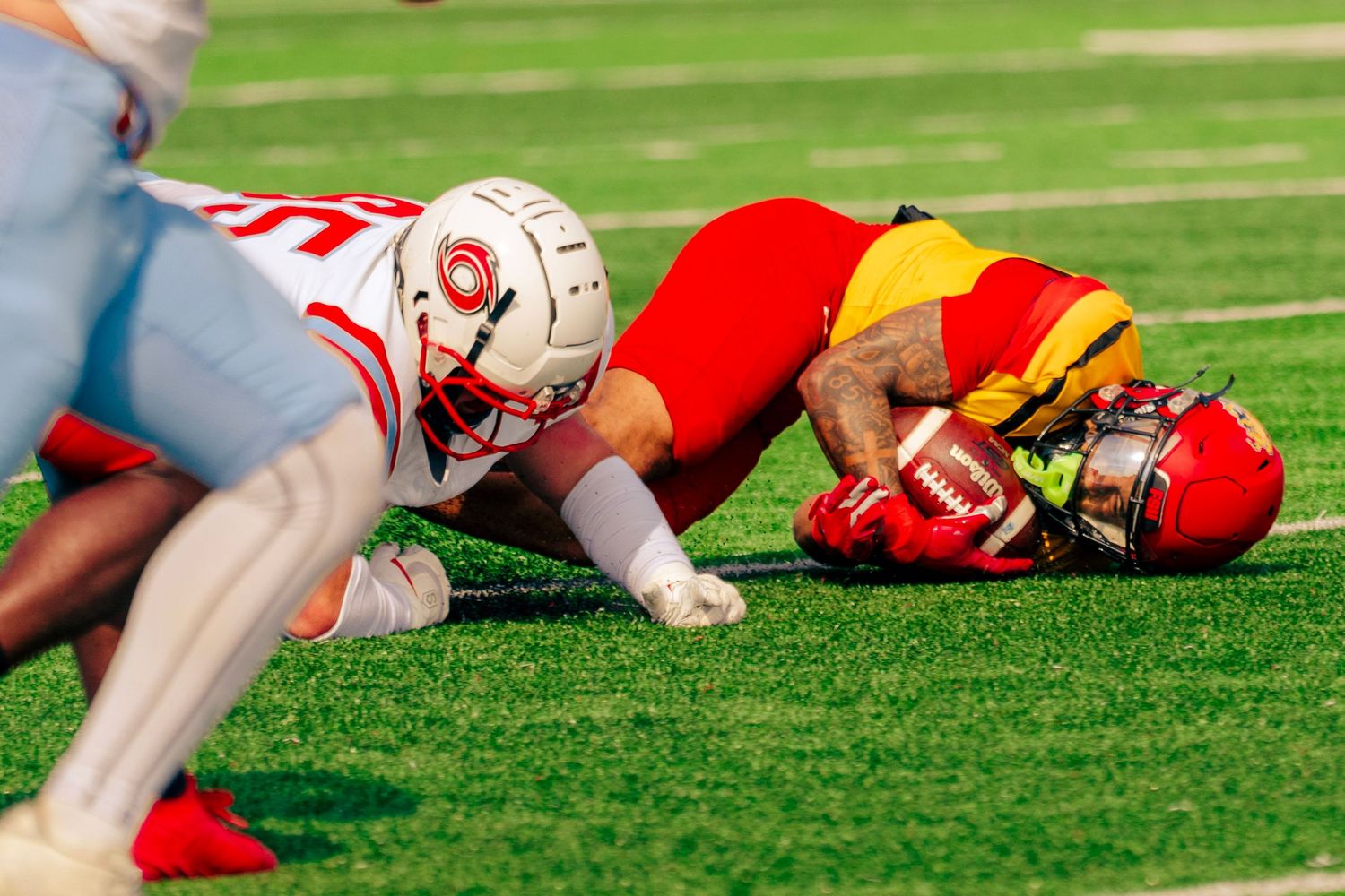 Football players dive and tackle on a green turf field during an intense game play.