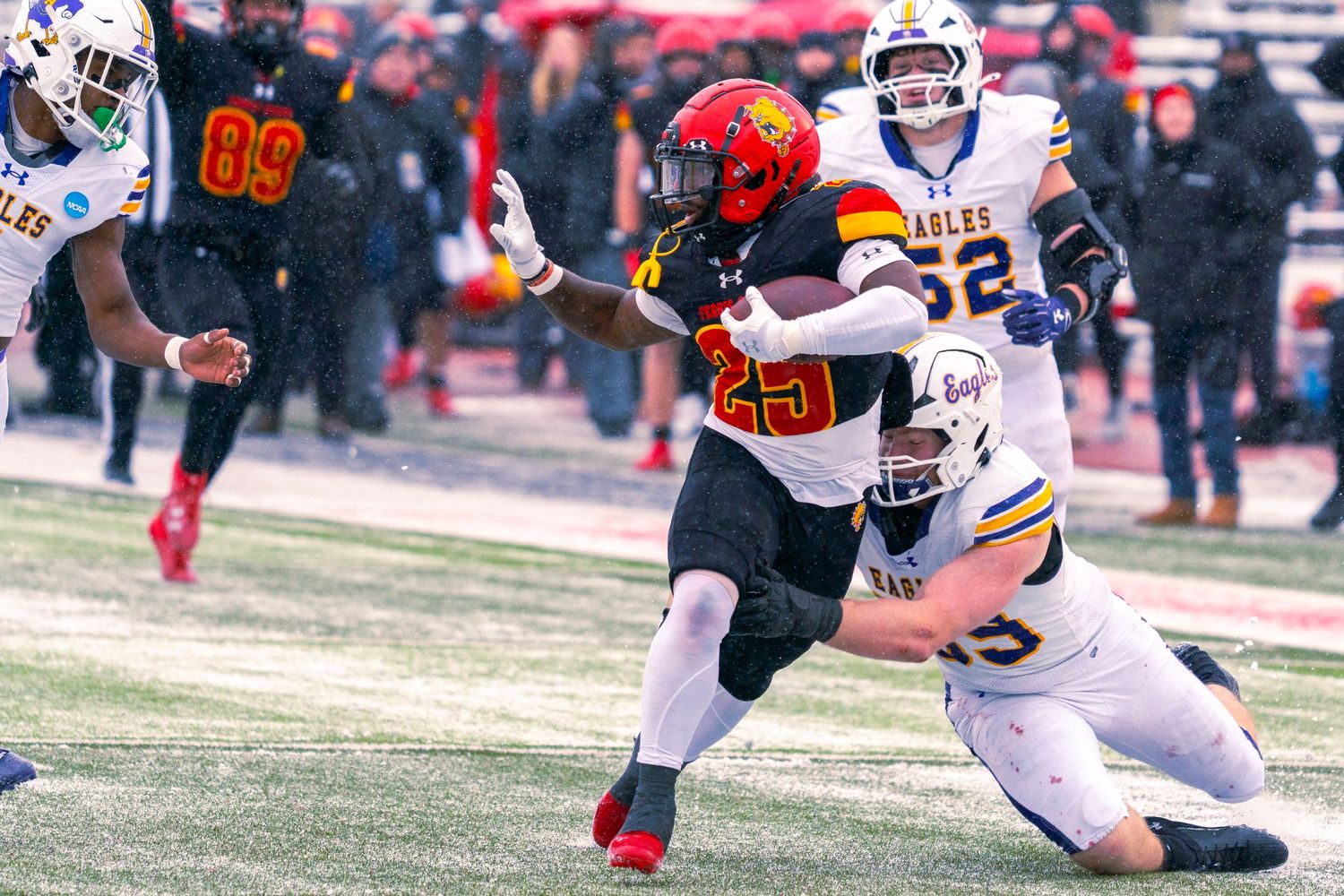 A football player in white and orange uniform breaks away from defenders during a game on a grass field.