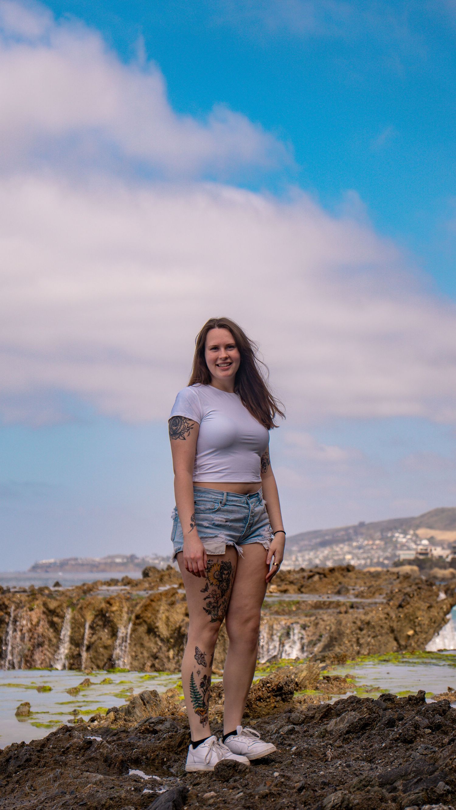 Individual in summer attire poses confidently on rocky ocean overlook.