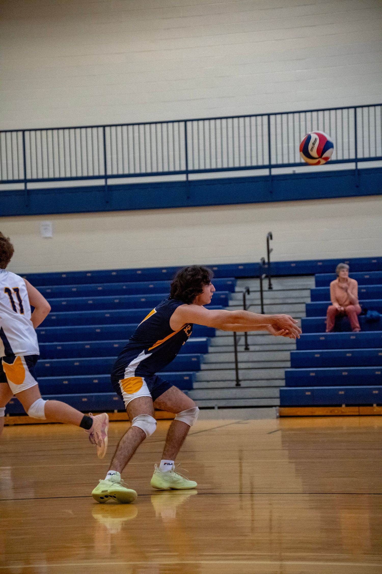 Volleyball player in navy uniform prepares to receive a serve during a match.
