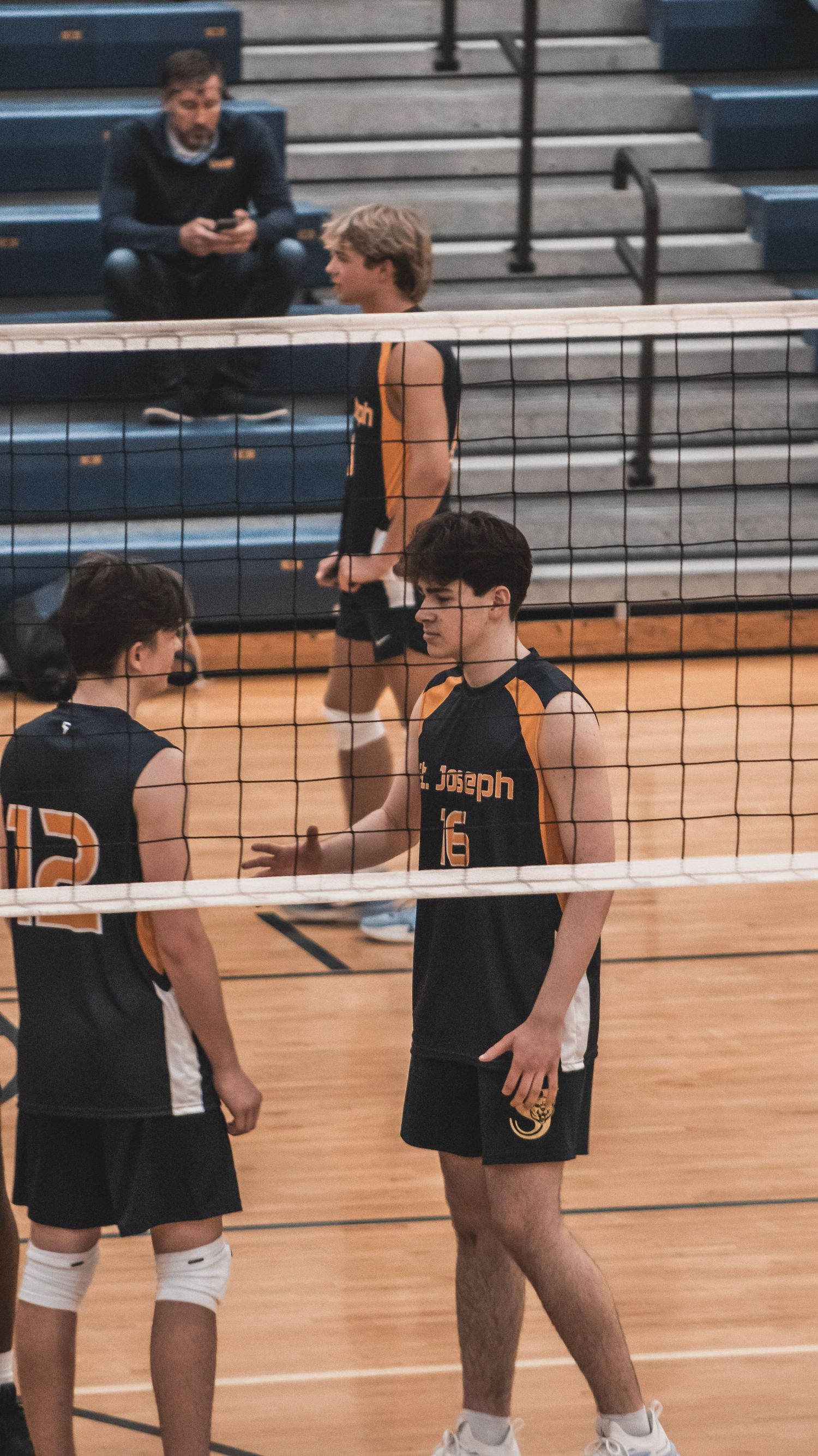 Players in black jerseys numbered 12 and 5 conversing at the volleyball net.