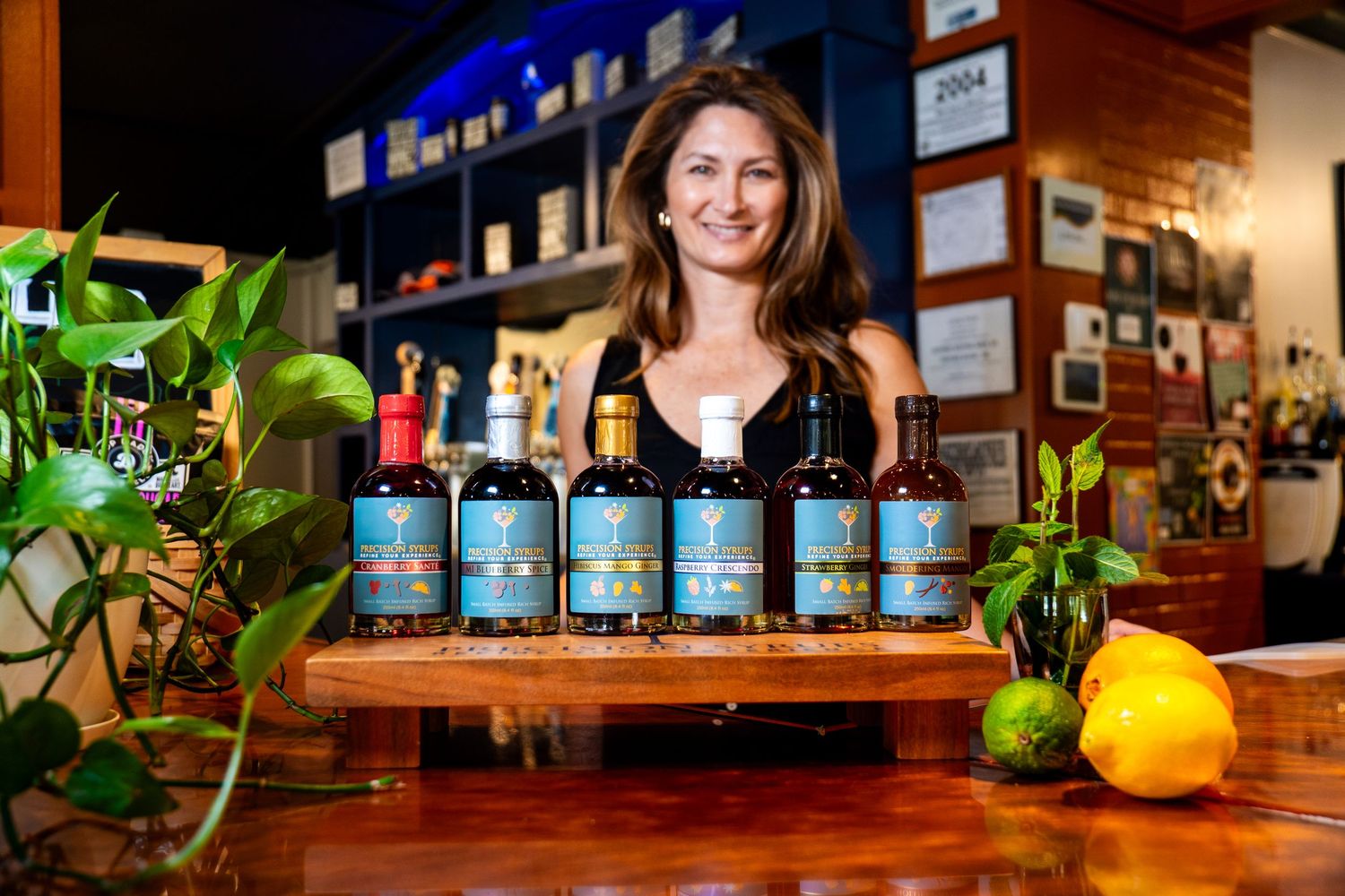 Multiple bottles of premium spirits displayed on wooden counter with fresh citrus garnish and greenery.