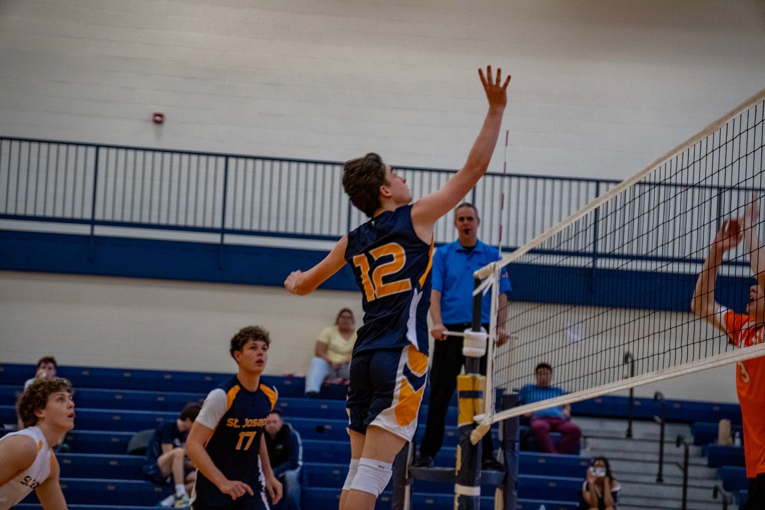 Indoor volleyball players leap in synchronized movement to block a spike at the net during an intense match.