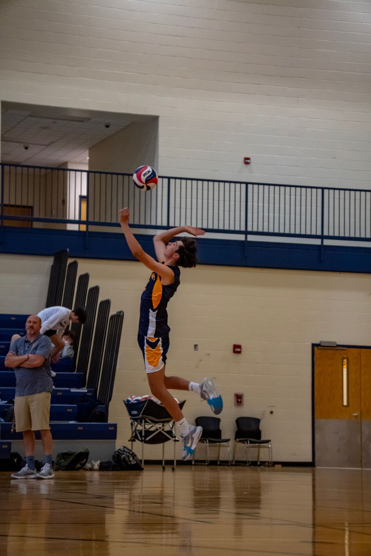 A volleyball player in navy and gold uniform leaps for a powerful serve.