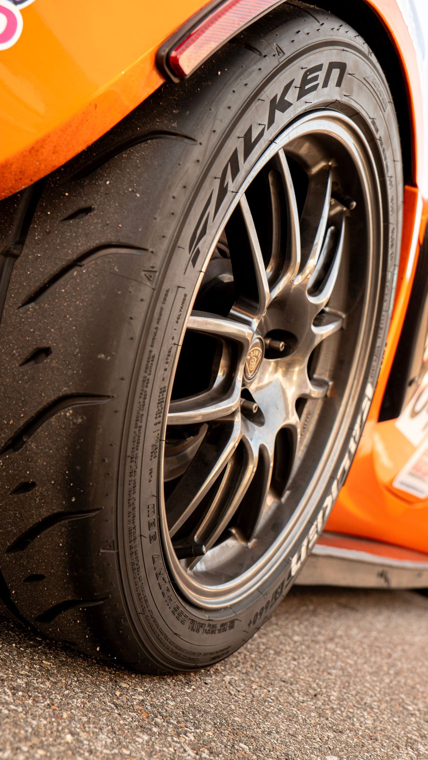 Close-up of a Falken performance tire and black multi-spoke wheel on orange car.