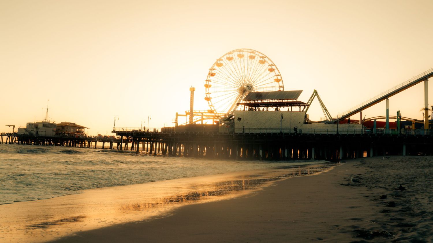 Dreamy sunset view of amusement park rides and pier stretching over ocean waves.