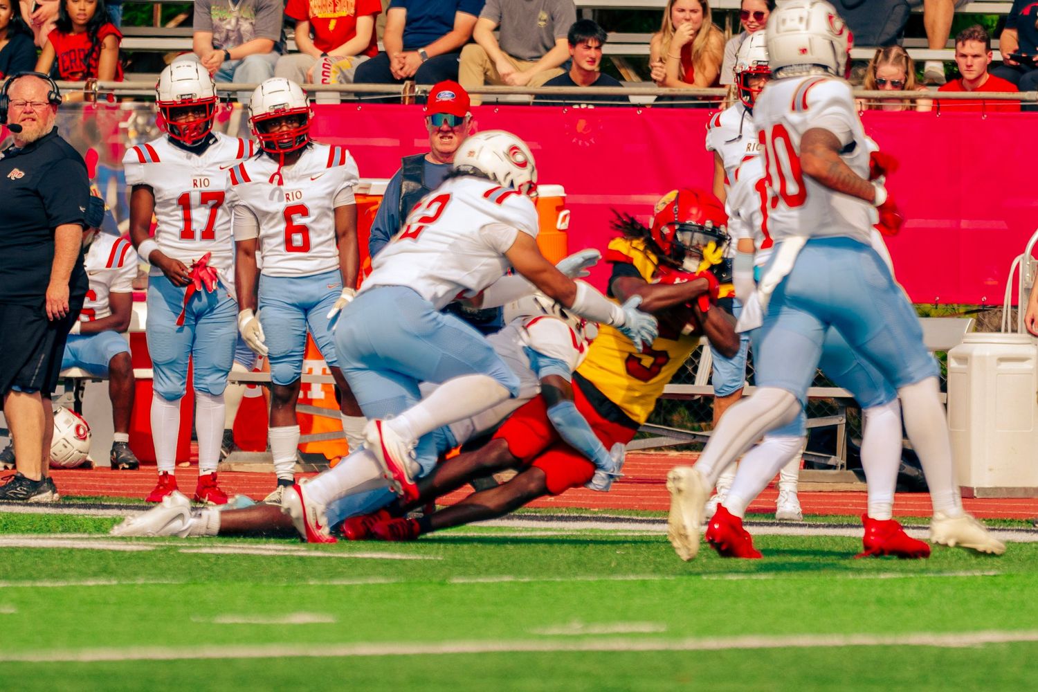 Football players dive for a loose ball during an intense goal line play at a stadium with red end zone turf.