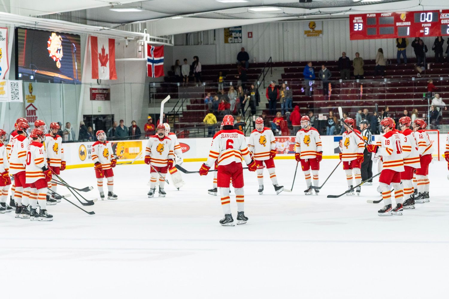 Hockey players in red and white uniforms line up on the ice during a pre-game ceremony at an indoor arena.
