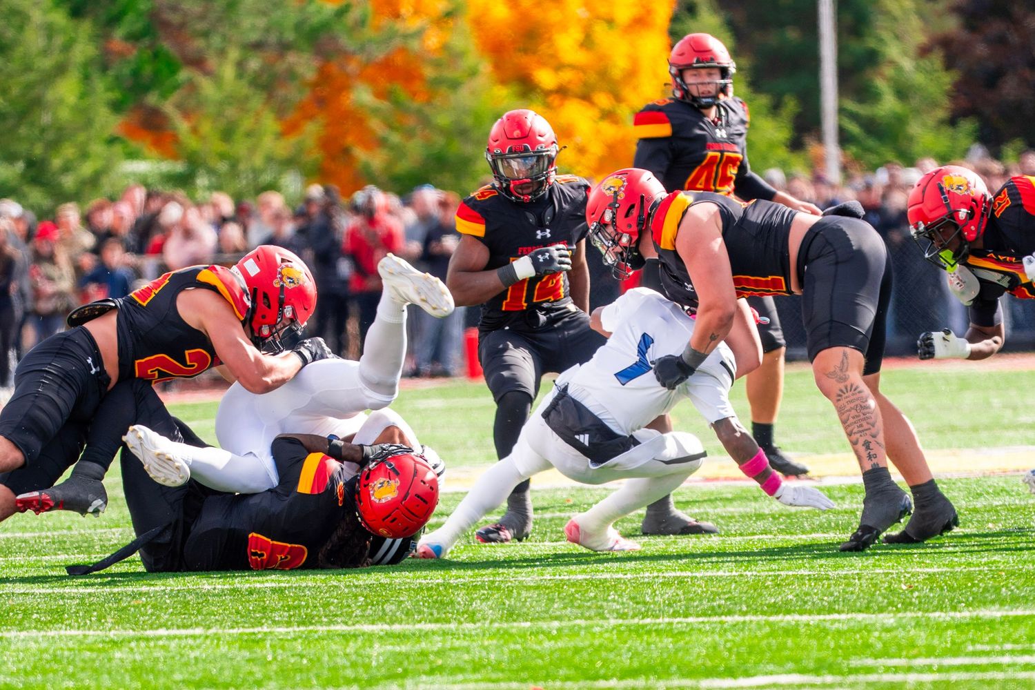 Football players in red and black uniforms collide with opposing team during intense gridiron action on autumn field.