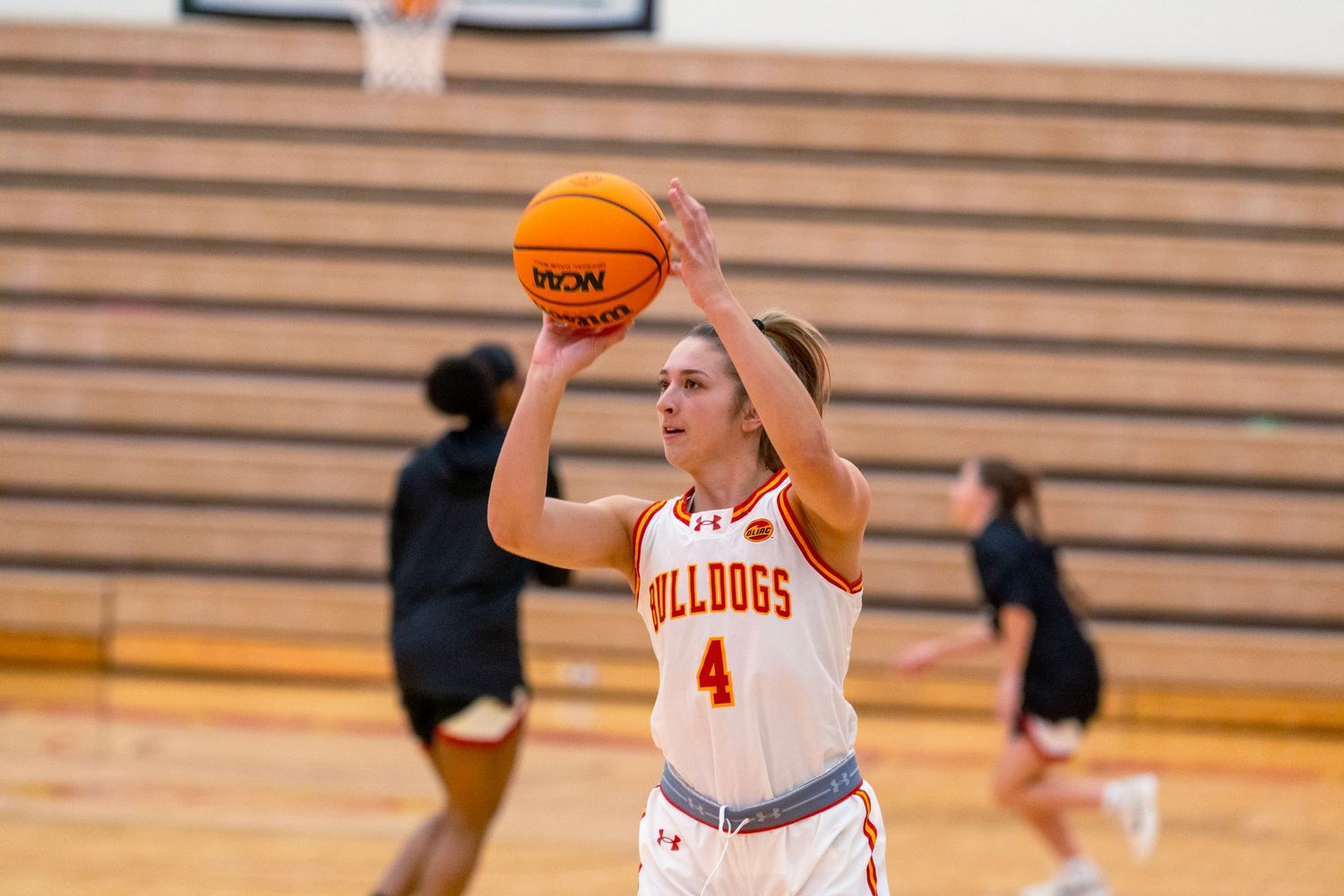 Basketball player in white jersey number 4 shoots the ball during a game in a wooden gymnasium.
