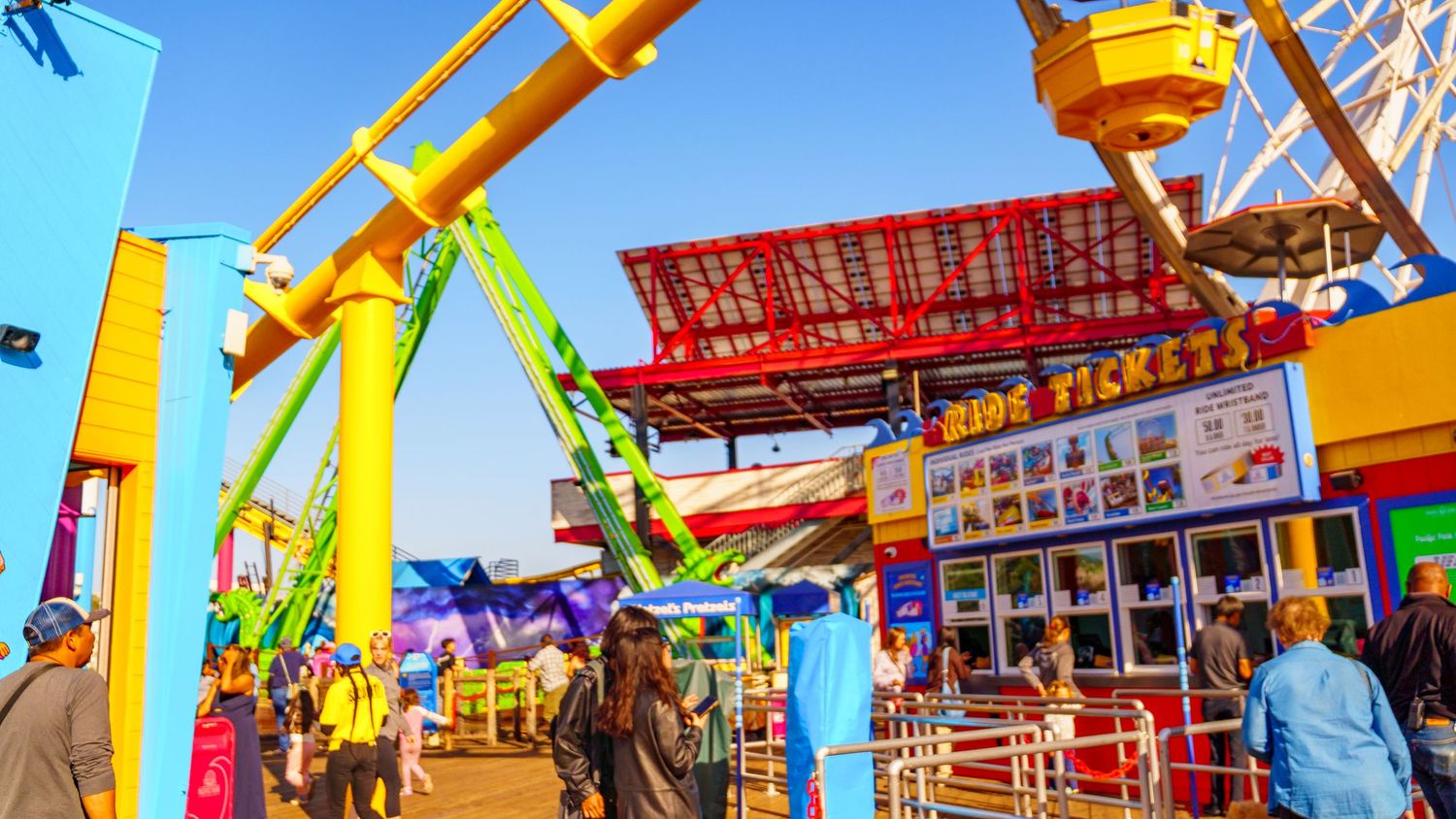 Colorful carnival rides and attractions fill the scene at an amusement park with vibrant reds, yellows and blues.