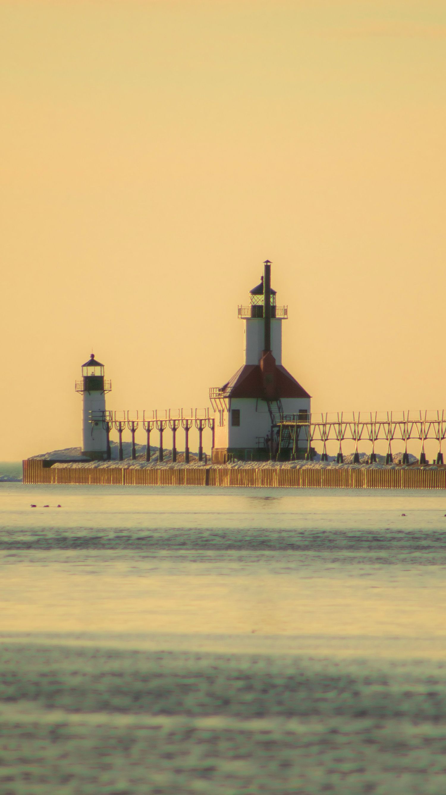Twin lighthouses of St. Joseph pier captured in soft golden morning light over Lake Michigan.