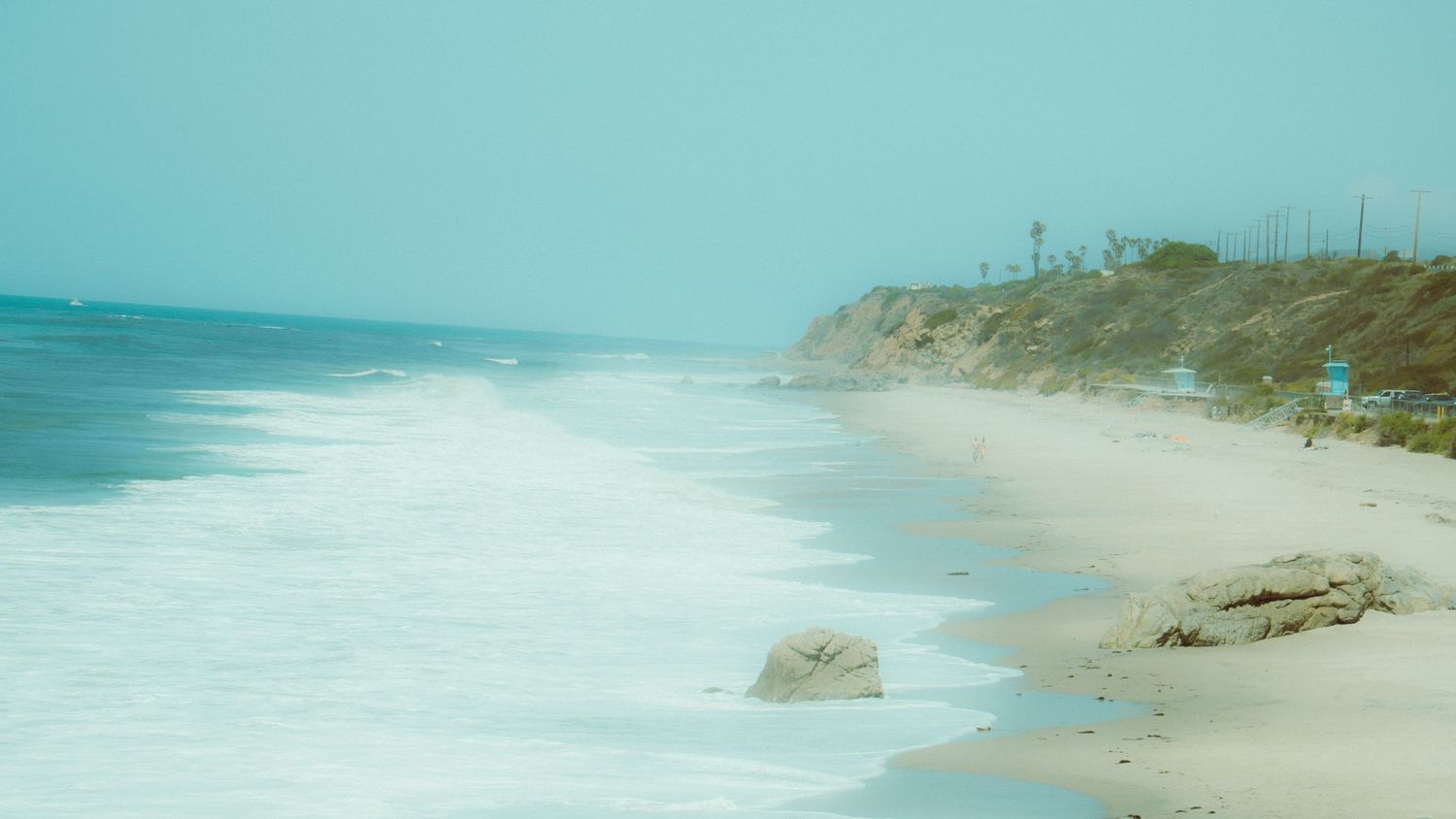 Sweeping coastal vista showing sandy beach meeting turquoise ocean waters.