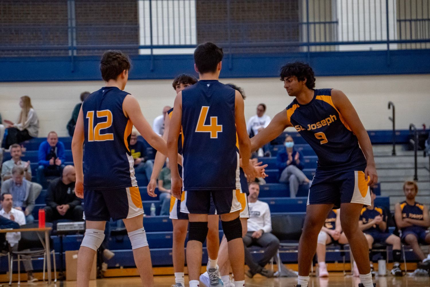 Three volleyball players in navy uniforms huddle during a game break.