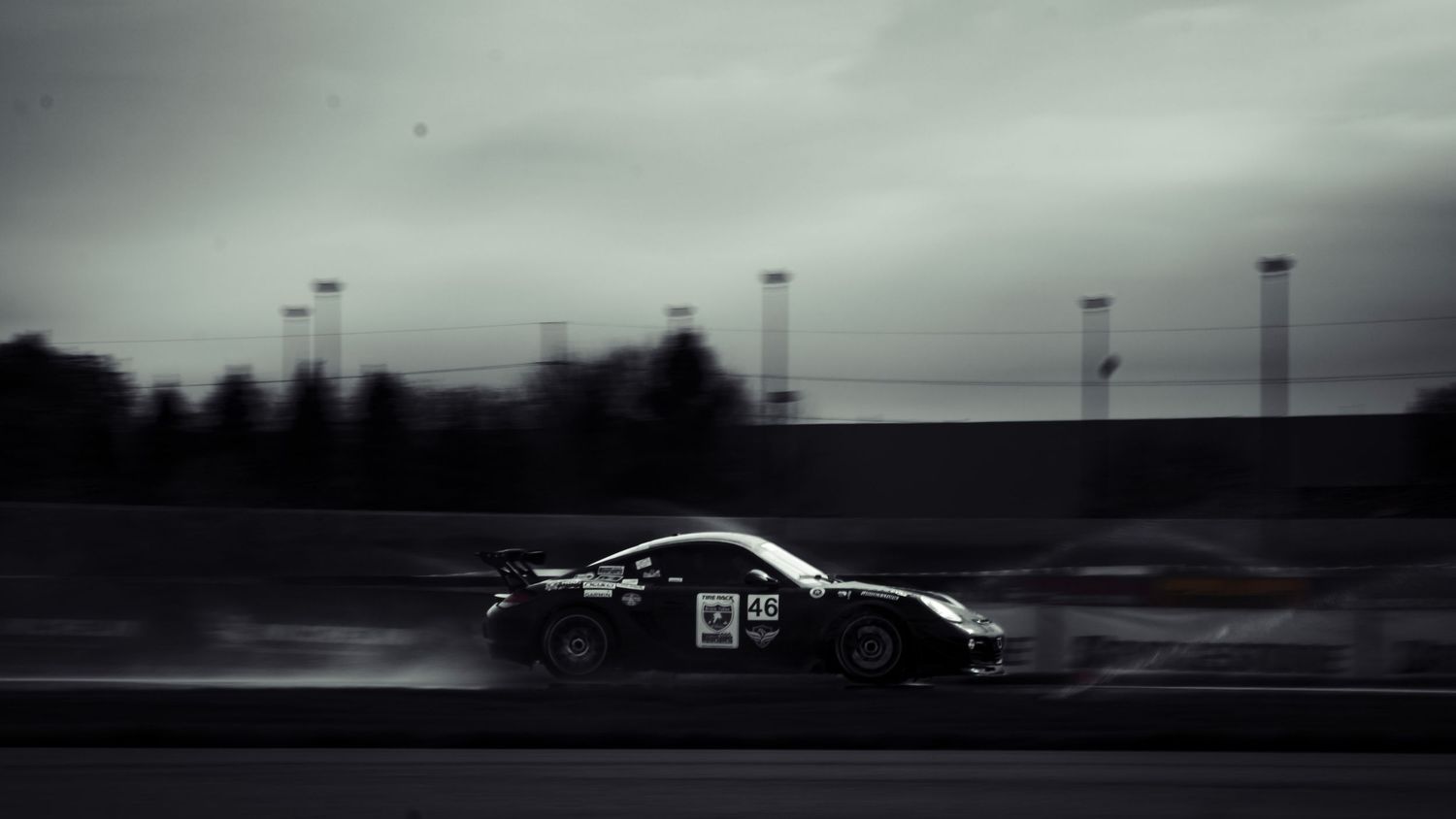 Race car creating dramatic spray on dark moody racetrack.
